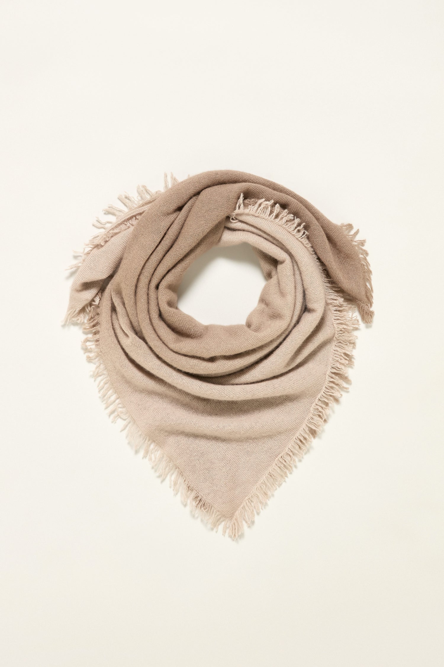 The Ombre Cashmere Square Scarf in beige is folded into a triangle and laid flat on a plain, light background, featuring soft cashmere and fringed edges.