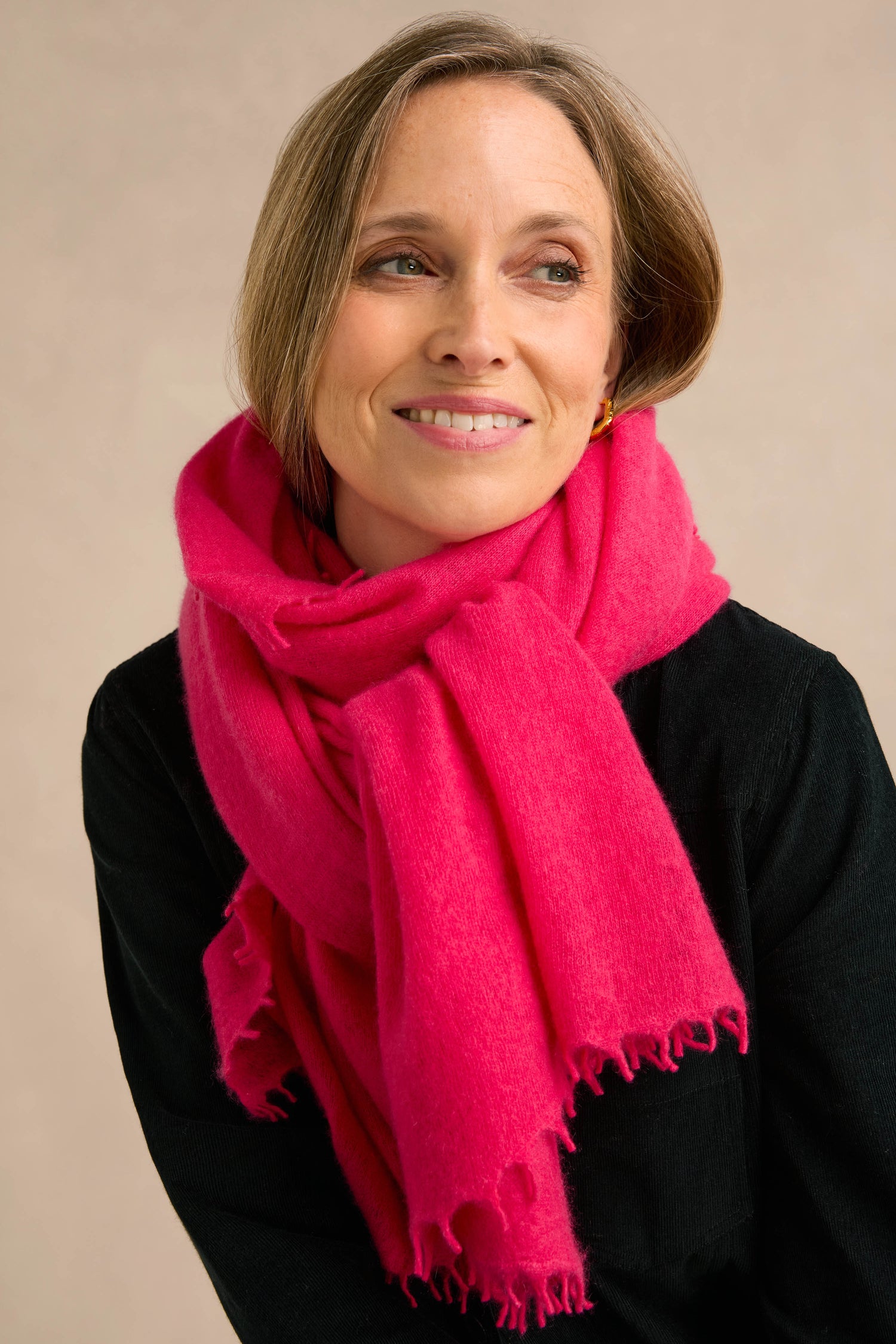 A person with short light brown hair, dressed in a black top and the Fuchsia Soft Cashmere Scarf, is smiling and looking slightly to the side against a plain background.