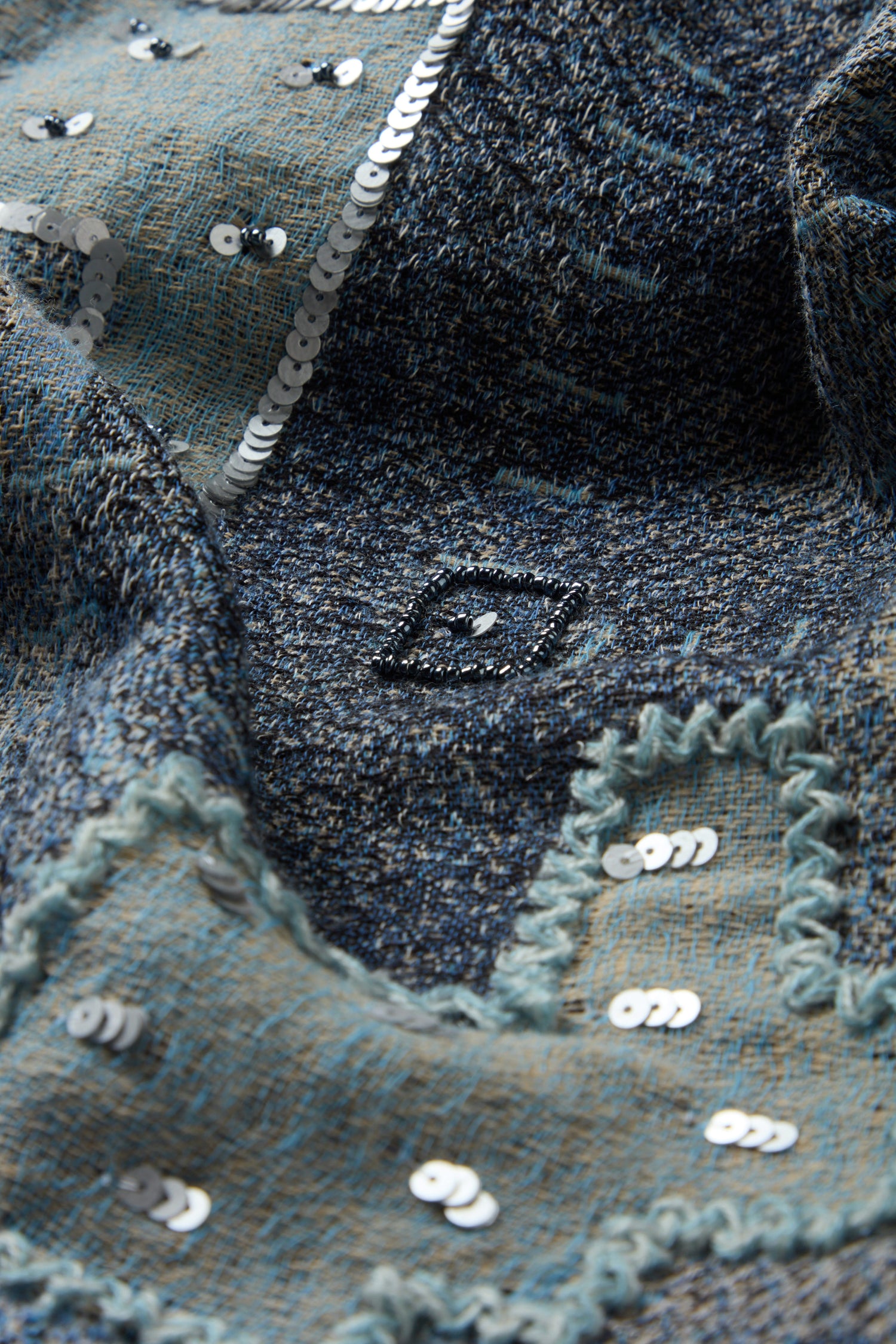 Close-up of the Etched Patchwork Sequin Wool Scarf showcasing textured blue wool with a patchwork design, embroidered patterns, a central diamond motif, and patches outlined in sequin accents and zigzag stitching.