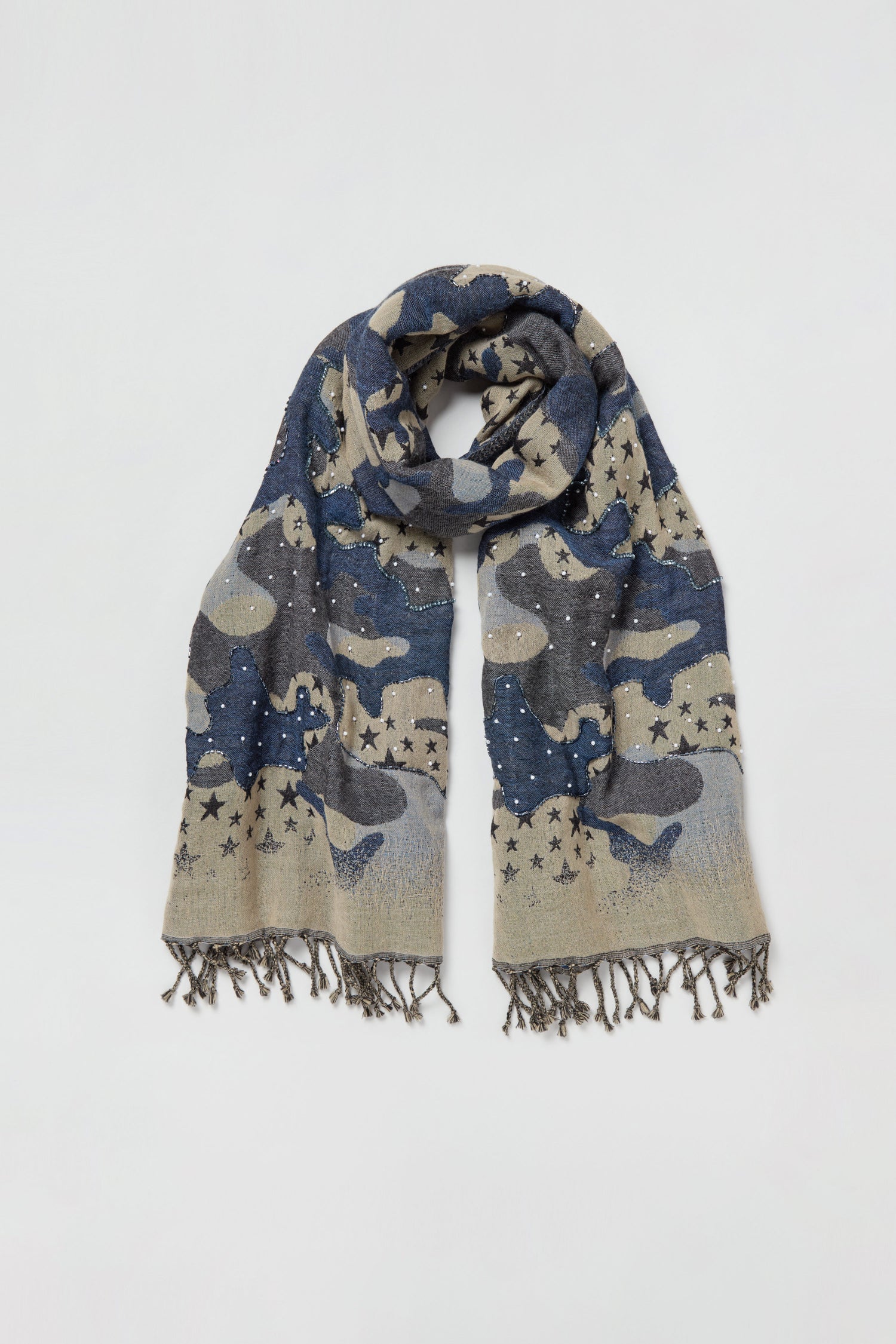 The Night Sky Sequin Wool Scarf, featuring a blue and beige camouflage pattern, star designs, sequin accents, small decorative studs, and fringed edges, is laid flat on a white background.