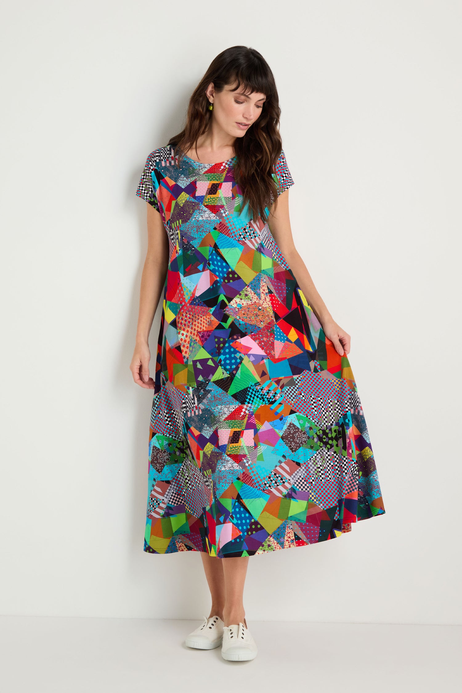 Woman wearing the Quilt Print Flared Dress, featuring a colorful geometric pattern and short sleeves, styled with white sneakers and standing against a plain white background.