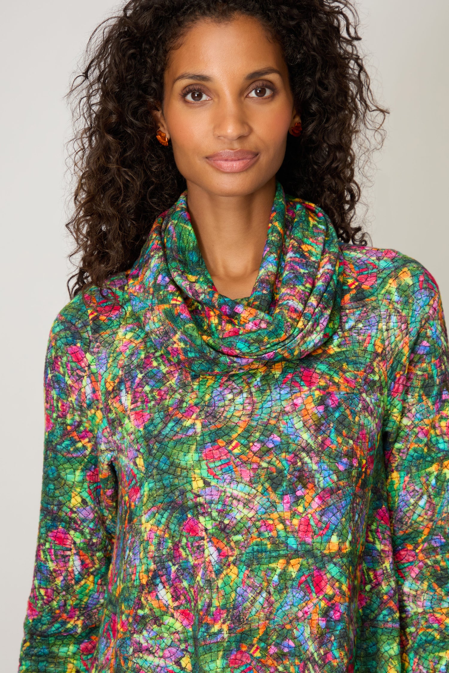A woman with curly hair wears a colorful mosaic-patterned top and a Circle Textured Snood, standing against a plain background.