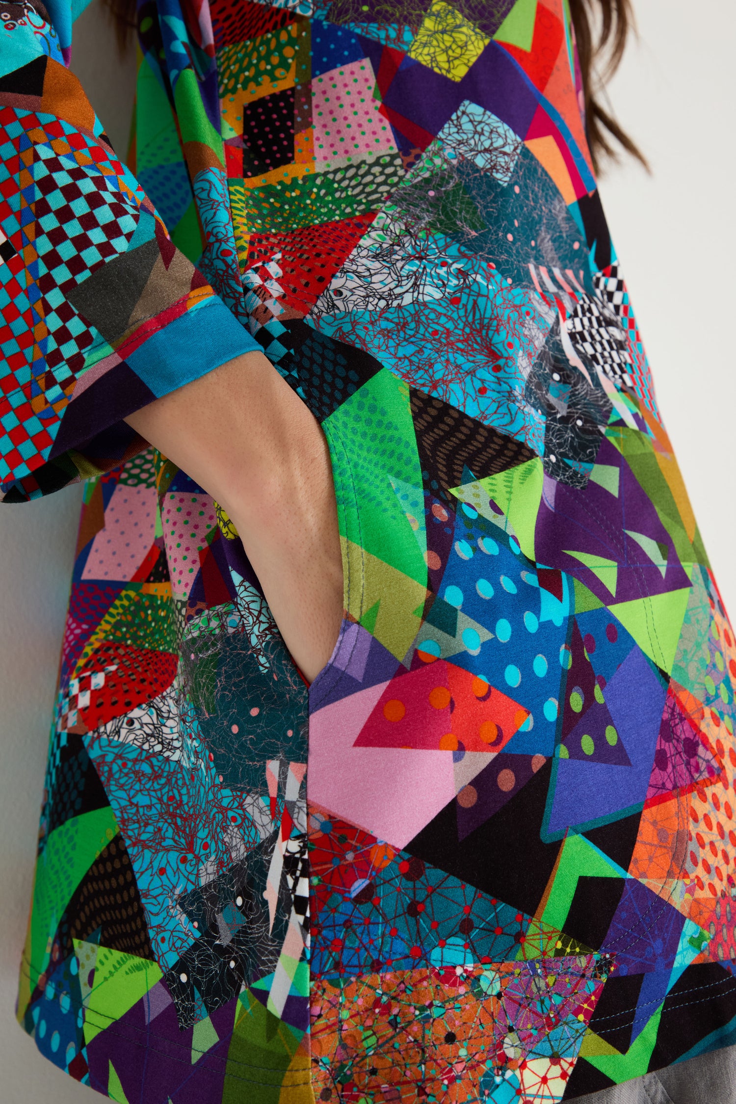 Person wearing the Quilt Print Flared Top, a long-sleeved stretch jersey garment with a geometric quilt print and side pocket.