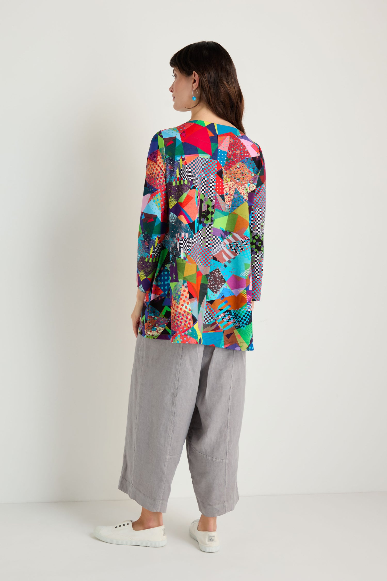 A person stands facing away, wearing the Quilt Print Flared Top with geometric patterns, paired with wide gray flared pants and white sneakers, set against a plain white background.