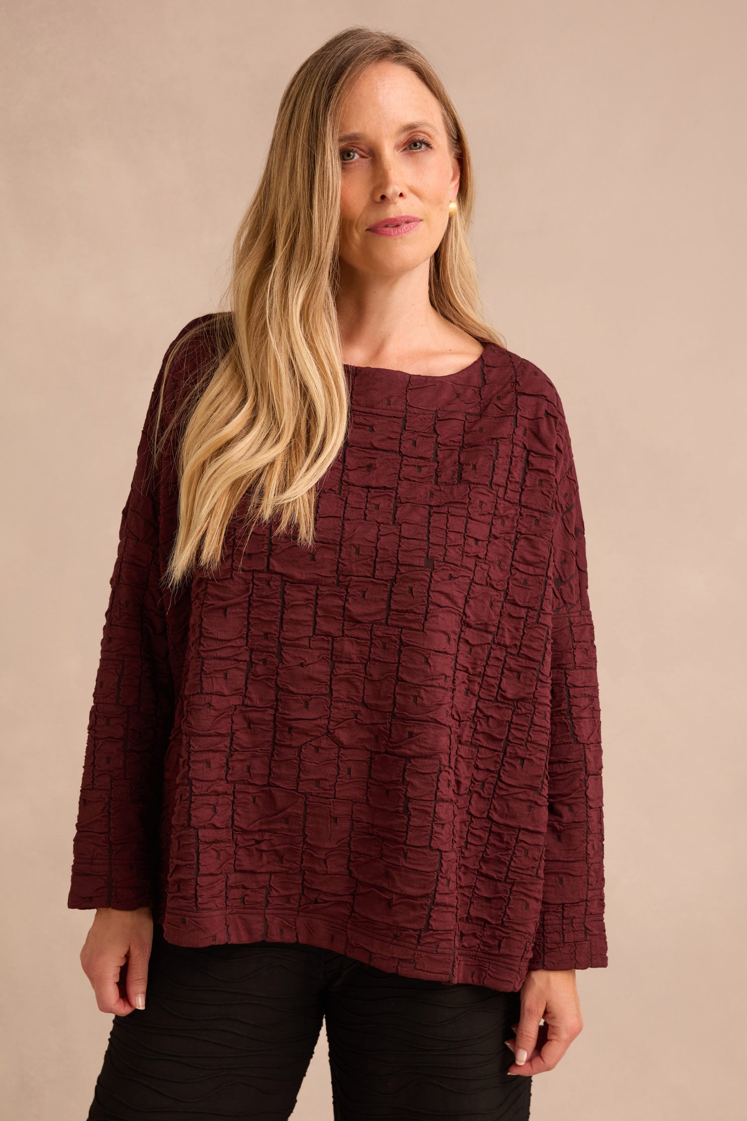 A woman with long blonde hair wears the Bordeaux Textured Squares Jersey Boxy Top paired with black pants, standing against a plain beige background.