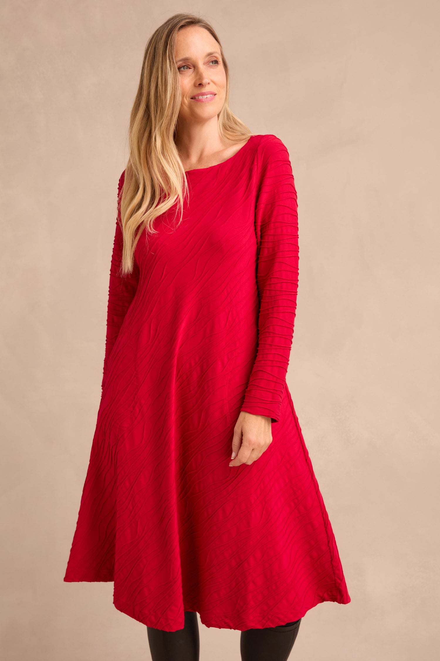 A woman wearing the Wave Textured Jersey Flared Dress in red, featuring long sleeves and a textured design, stands against a neutral background, looking slightly to the side.