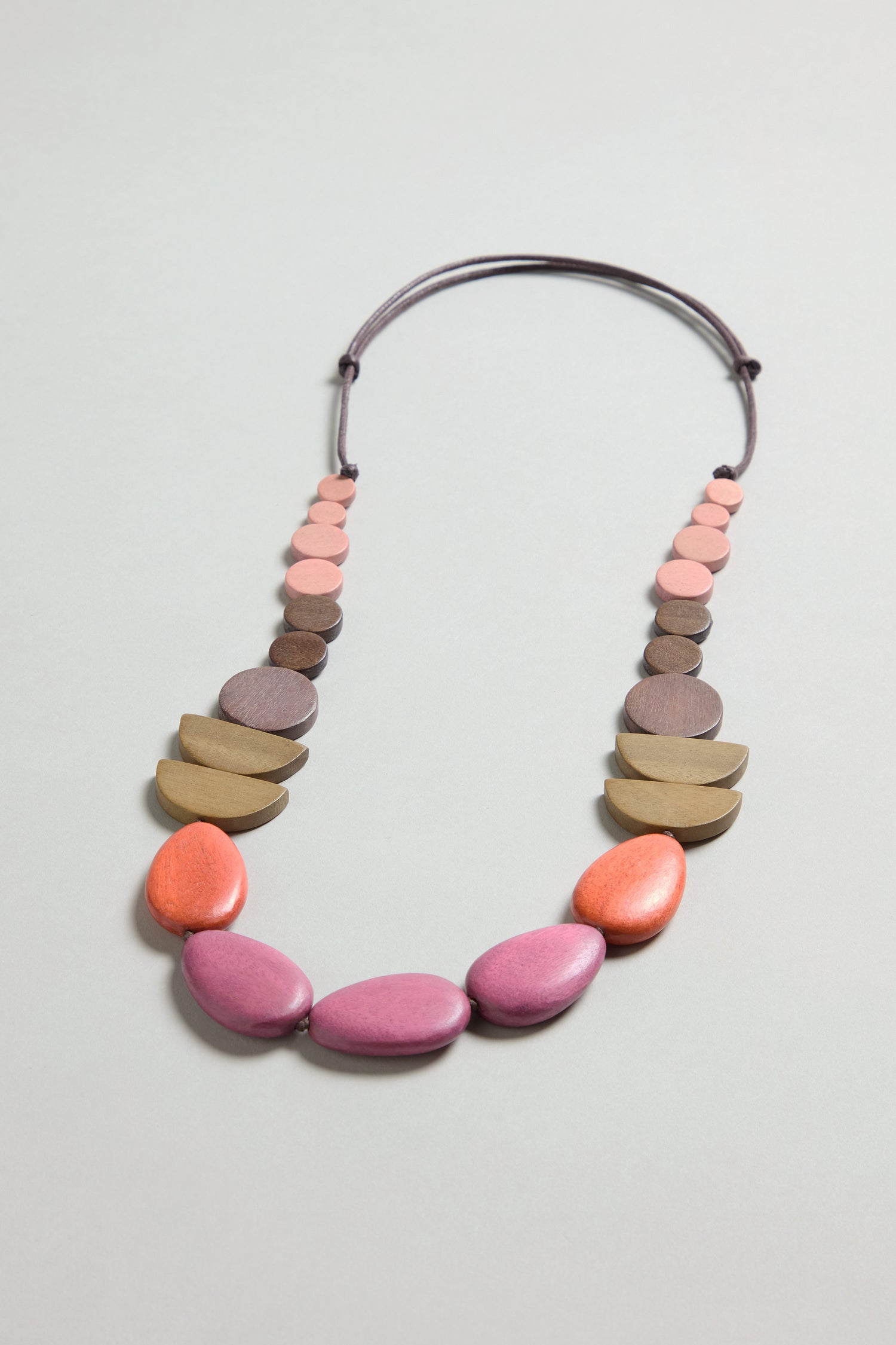 Make a statement with the Assorted Wooden Shapes Necklace, featuring bold pink and orange oval beads in front, accented by smaller brown and tan half-round beads on an adjustable cord.