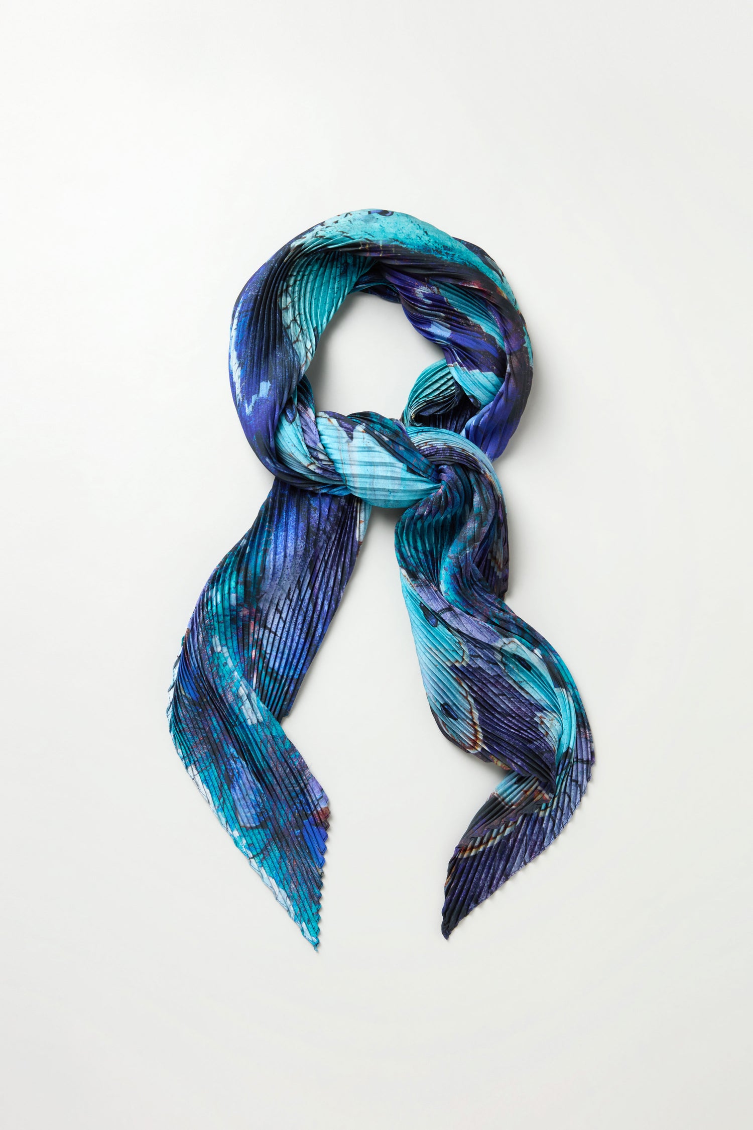 The Butterfly Pleat Scarf in blue features a pleated satin design on a white background, making it a perfect lightweight statement accessory.