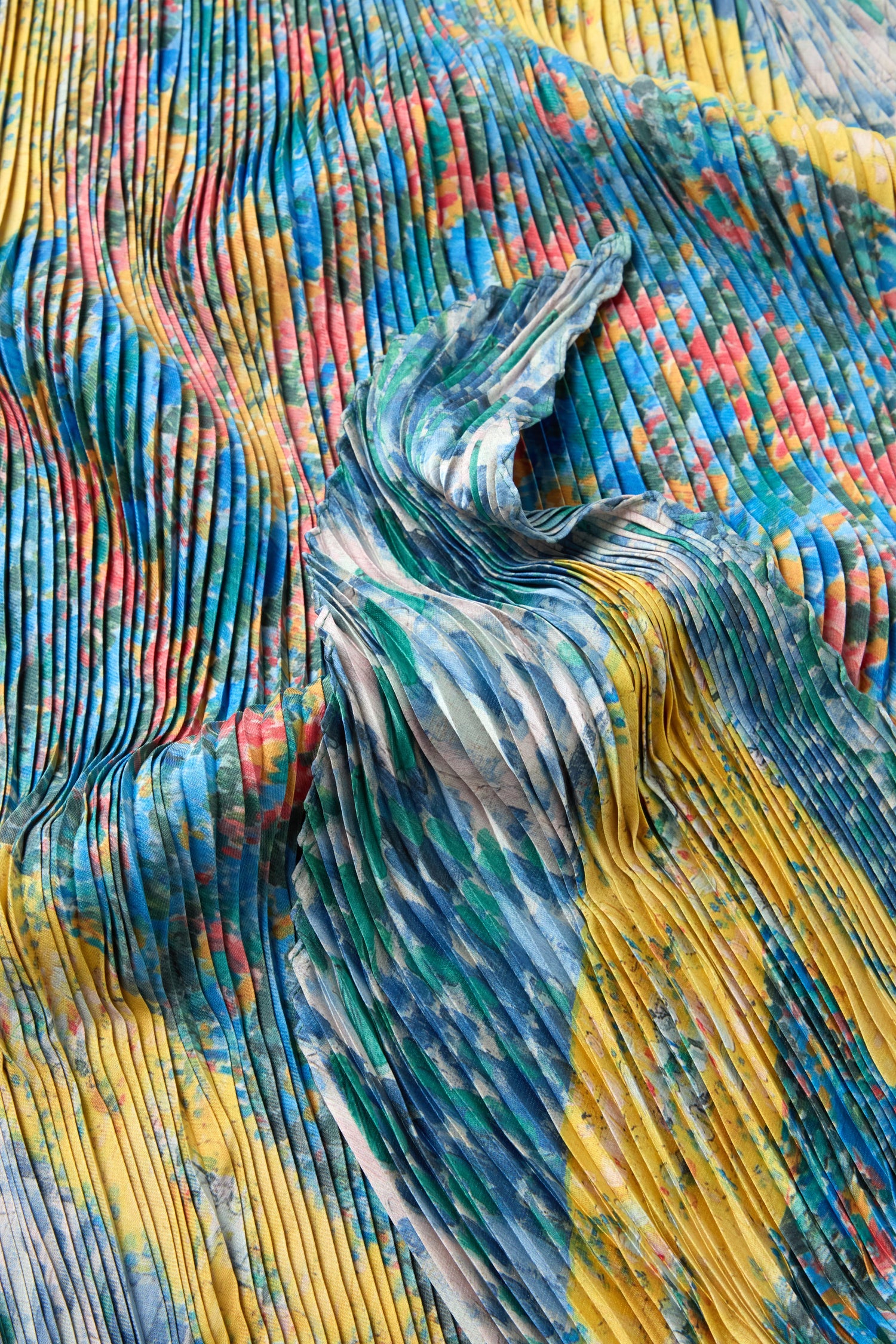 Close-up of the Artistry Pleat Scarf, showcasing its pleated satin texture and vibrant multicolored pattern in blue, yellow, green, and red. Lightweight and eye-catching—ideal as a bold accessory for versatile styling.