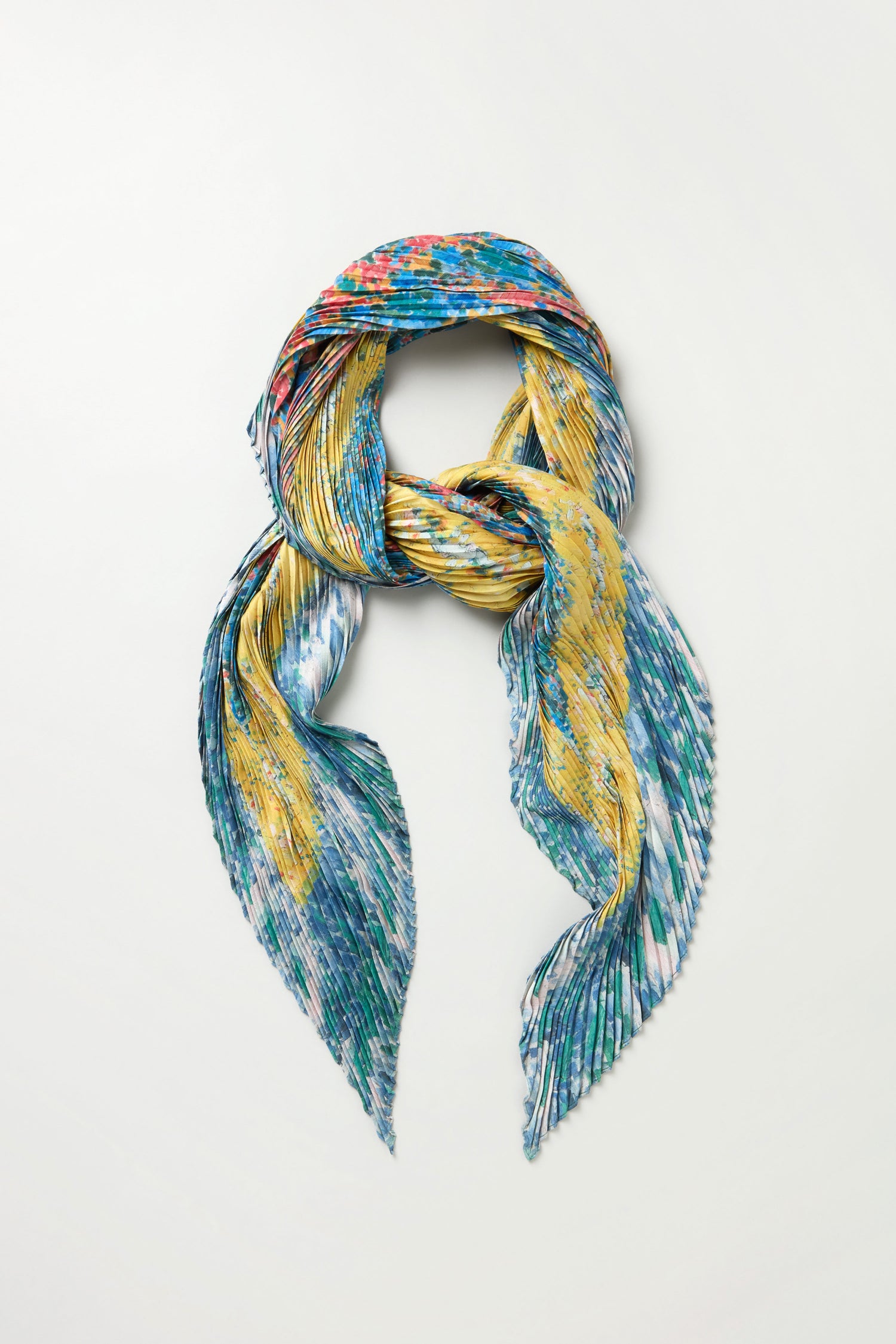 The Artistry Pleat Scarf features a colorful abstract pattern in blue, yellow, green, and red on satin, styled in a loose knot on a white background—a lightweight statement piece ideal for versatile looks.