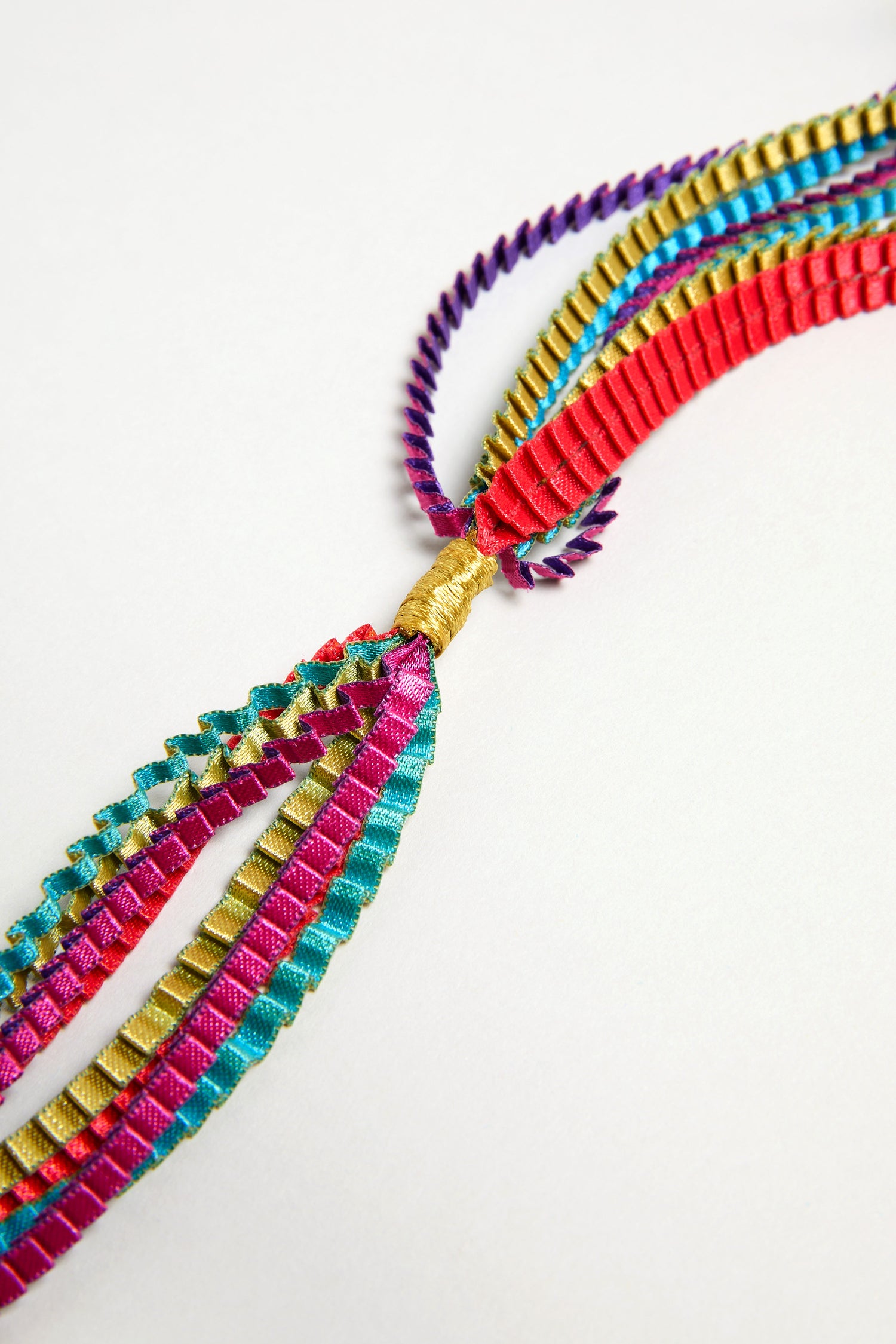 The Long Pleated Necklace features twisted satin ribbons in teal, pink, purple, red, and gold, knotted at one end for a bold look. Presented against a plain white background.