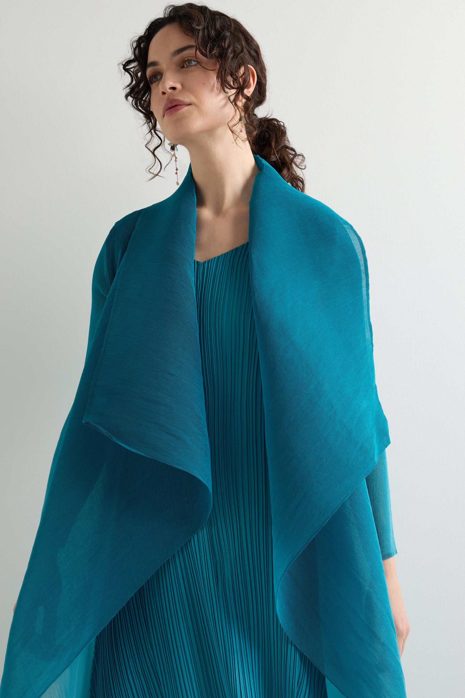 A person models the Pleat Jacket in teal, radiating bohemian flair with its pleated design and matching draped shawl against a plain white background.