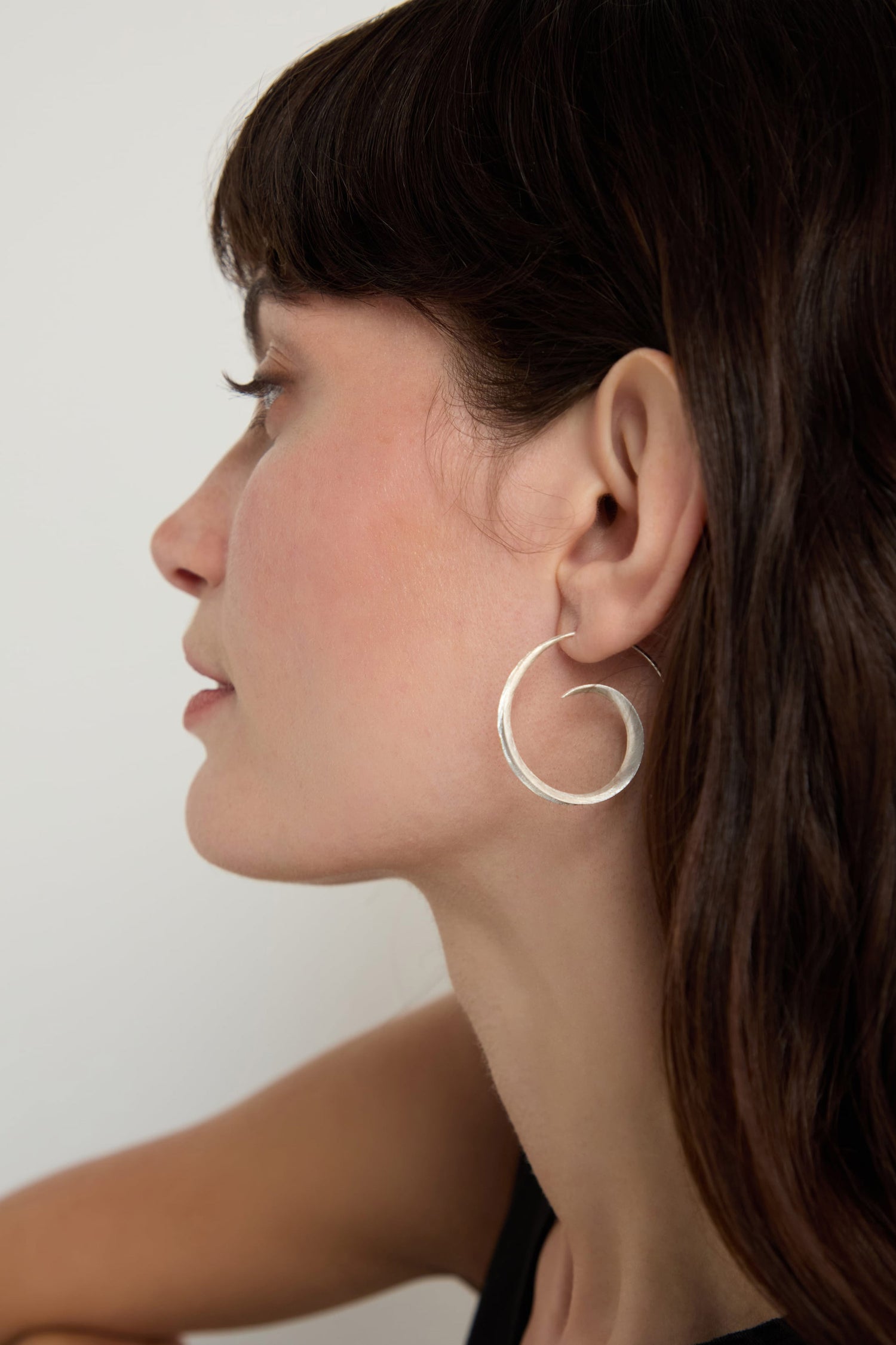 A woman with long brown hair is shown in profile, wearing Silver Swirl Earrings that catch the light with their sculptural design.