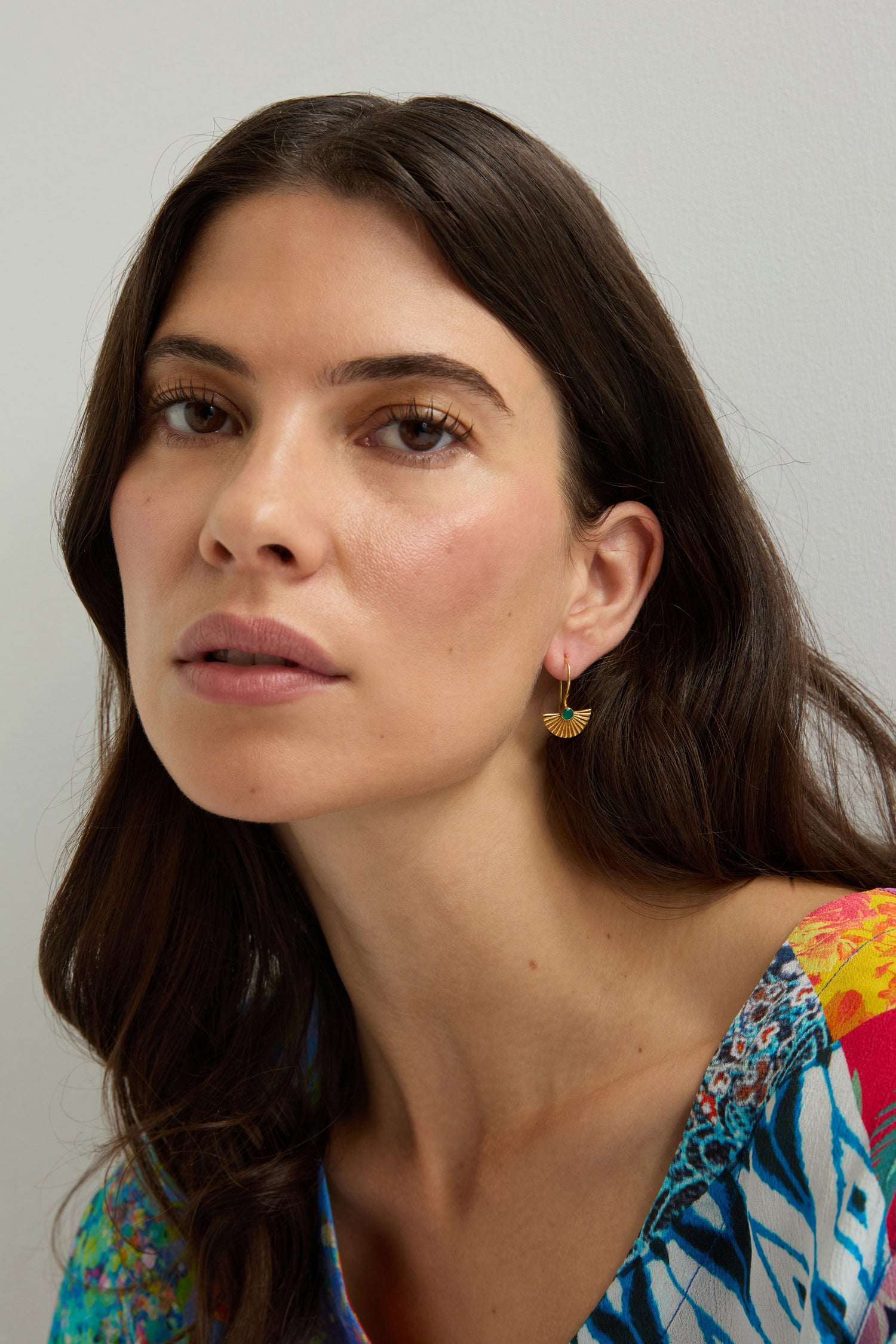 A woman with long brown hair wears a colorful patterned top and Gold Vermeil Onyx Fan Earrings, looking at the camera against a plain light background.