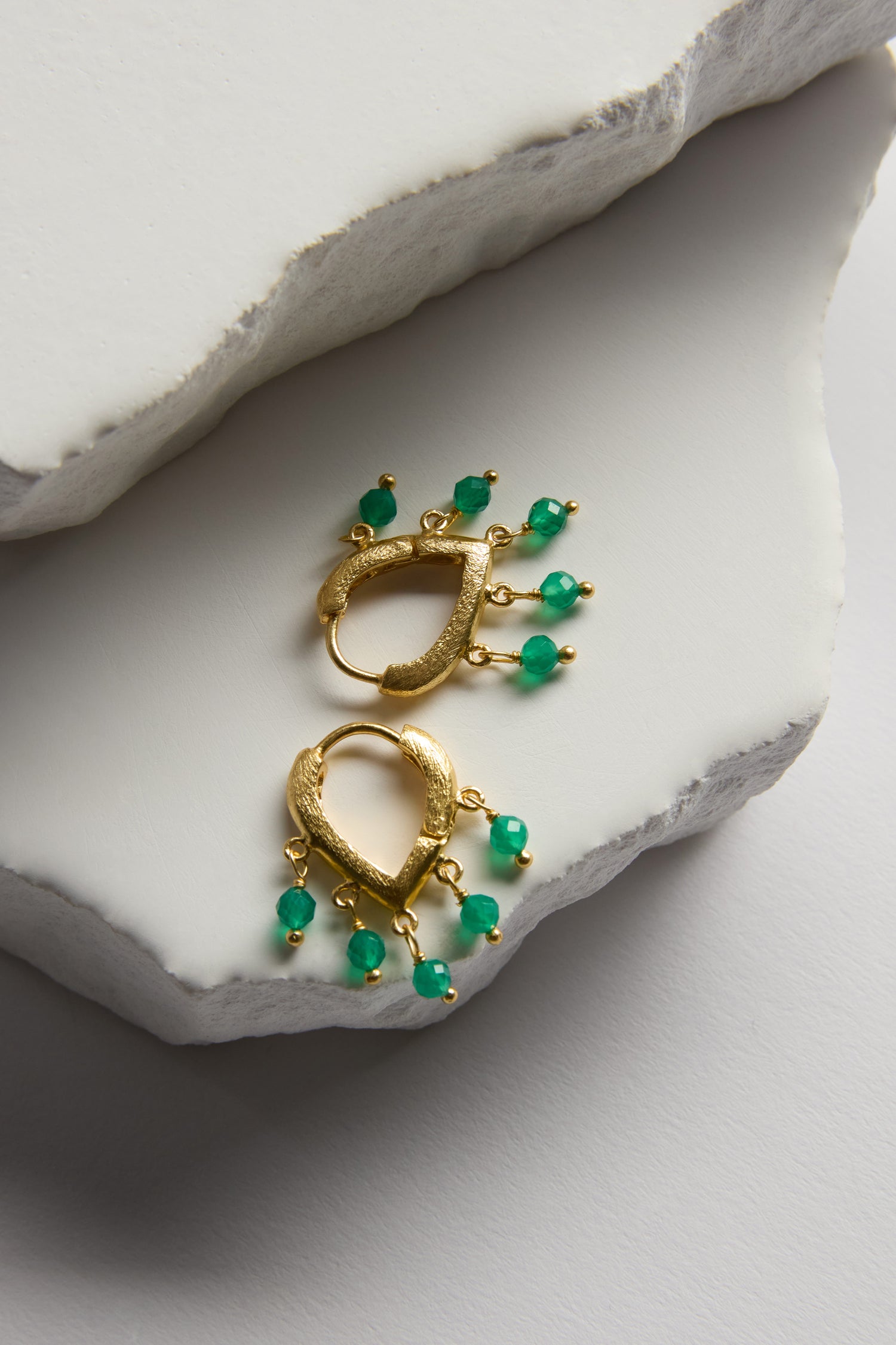 Gold Vermeil Onyx Teardrop Hoops with green bead dangles displayed on white textured stone slabs.