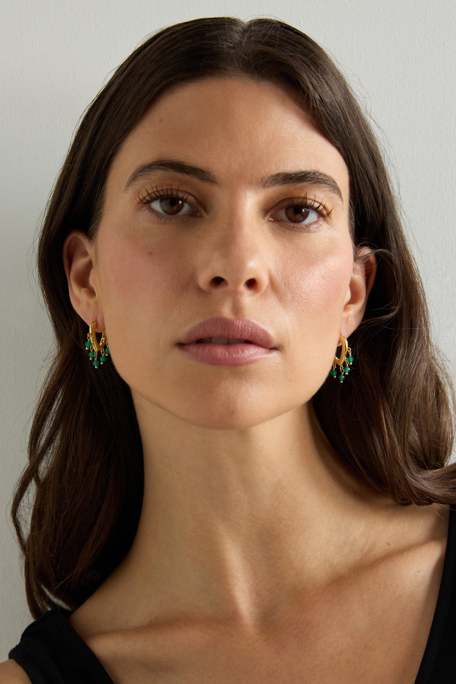 A woman with long brown hair wears a black top and the Gold Vermeil Onyx Teardrop Hoops, looking directly at the camera against a plain light background.
