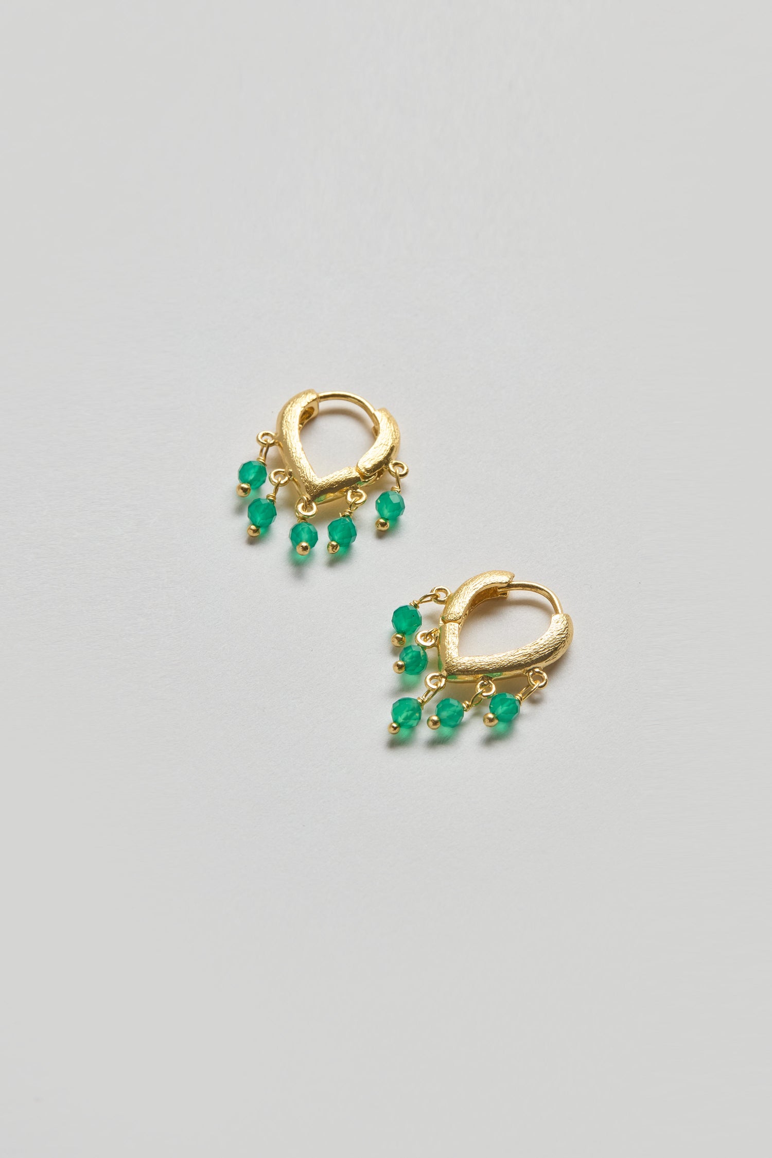 The Gold Vermeil Onyx Teardrop Hoops are pictured on a light gray background, featuring a pair of gold vermeil hoops each adorned with five small green beads.