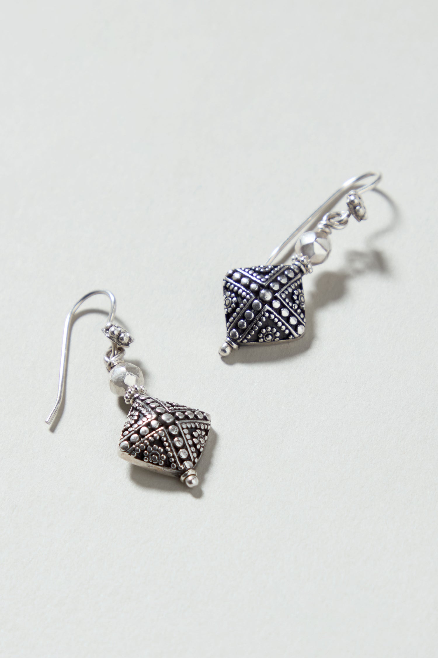 Silver Faceted Drop Earrings featuring geometric, textured designs are displayed on a light background.