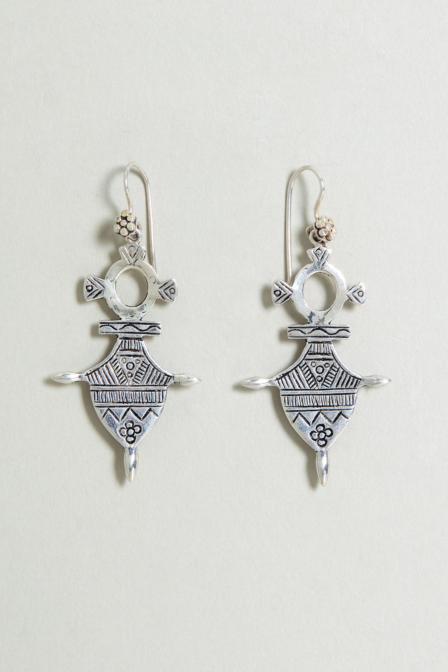The Silver Tuareg Earrings feature sterling silver with detailed geometric and floral engravings on a light background, inspired by classic Tuareg designs.