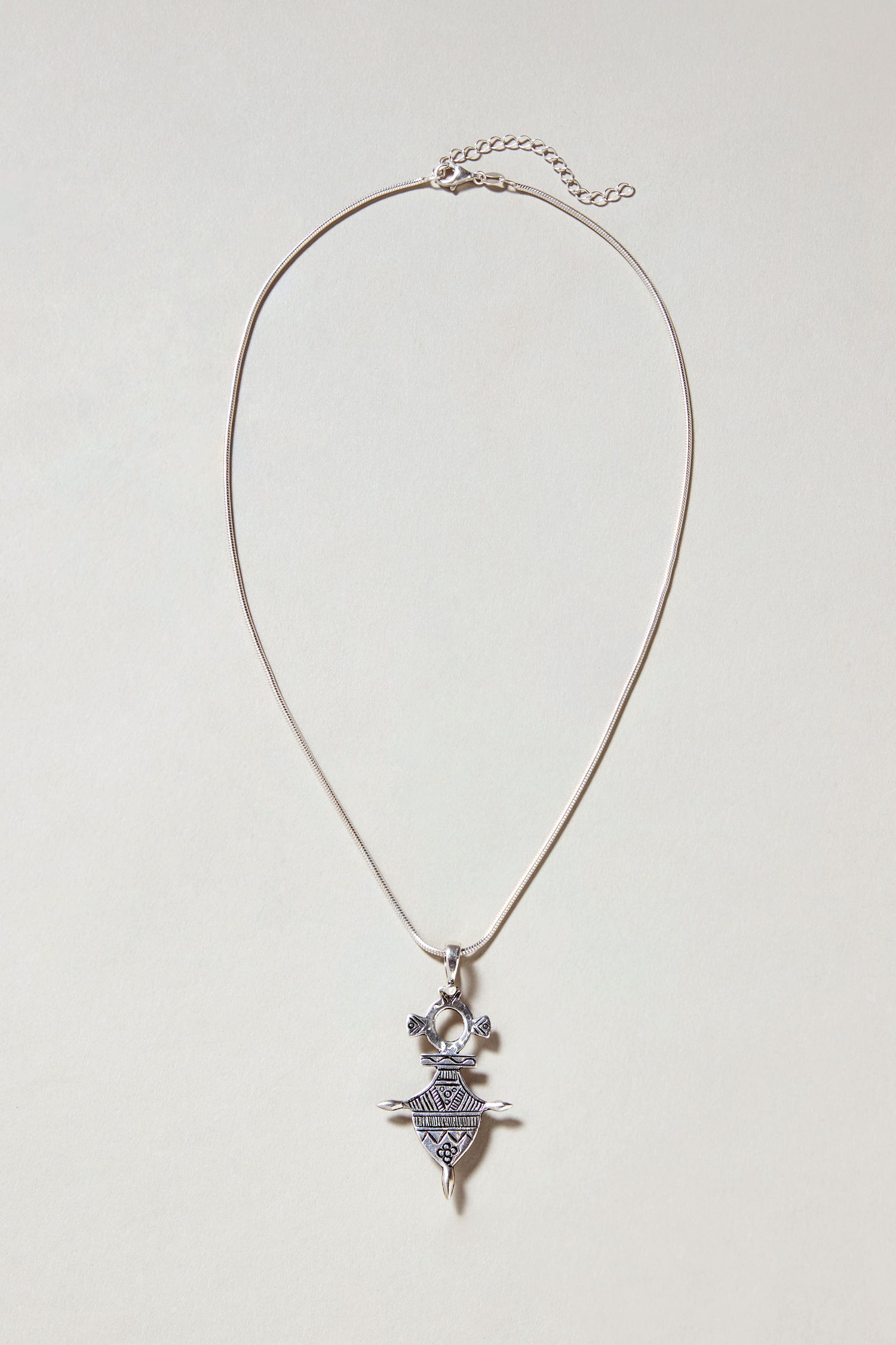 A Silver Tuareg Pendant with a geometric engraved design hangs from a thin silver chain, shown on a light background.