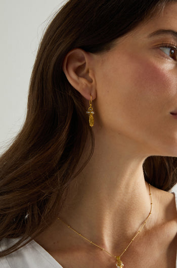A close-up of a woman's face and neck showcases Gold Vermeil Pearl Drop Earrings and a delicate gold necklace against a neutral background.