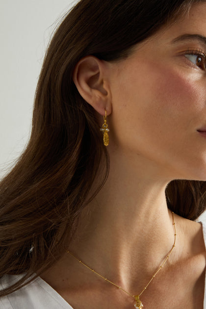 A close-up of a woman's face and neck showcases Gold Vermeil Pearl Drop Earrings and a delicate gold necklace against a neutral background.