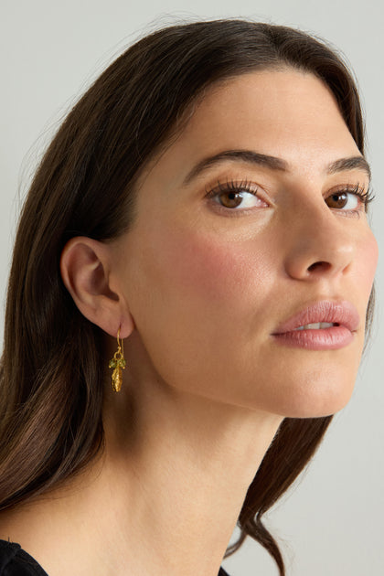 A woman with long brown hair and natural makeup wears Gold Vermeil Peridot Drop Earrings with a black top as she gazes slightly upward against a neutral background.