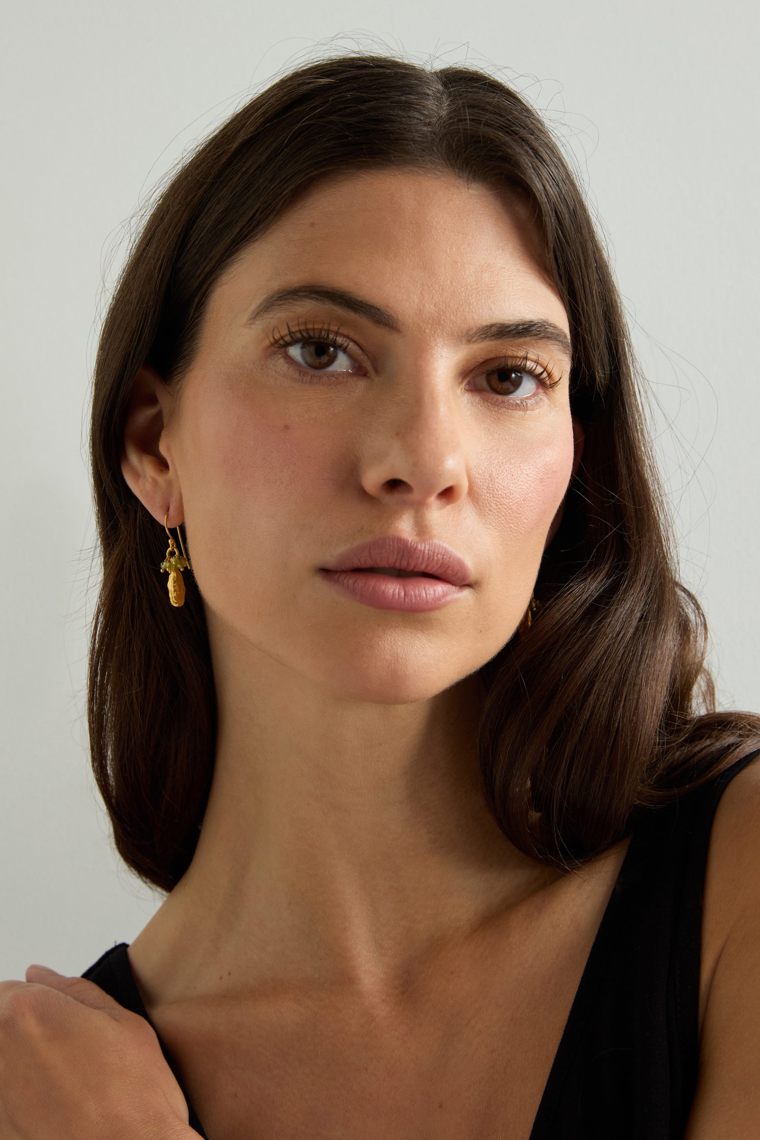 A woman with long brown hair wears Gold Vermeil Peridot Drop Earrings and a black top, looking directly at the camera against a plain light background.