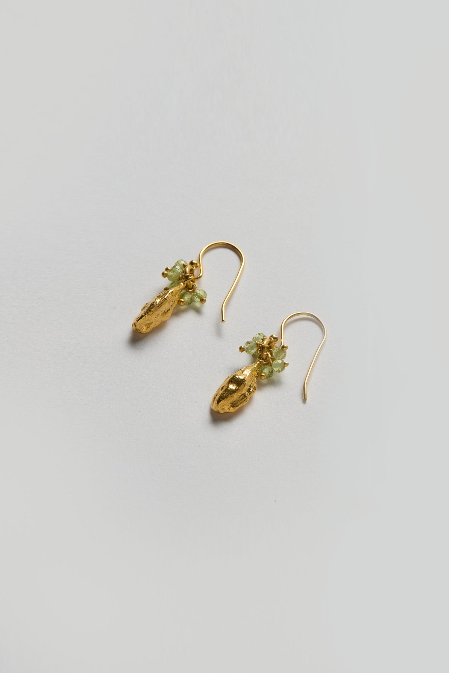 The Gold Vermeil Peridot Drop Earrings feature small green peridot bead clusters and are shown against a plain light background.