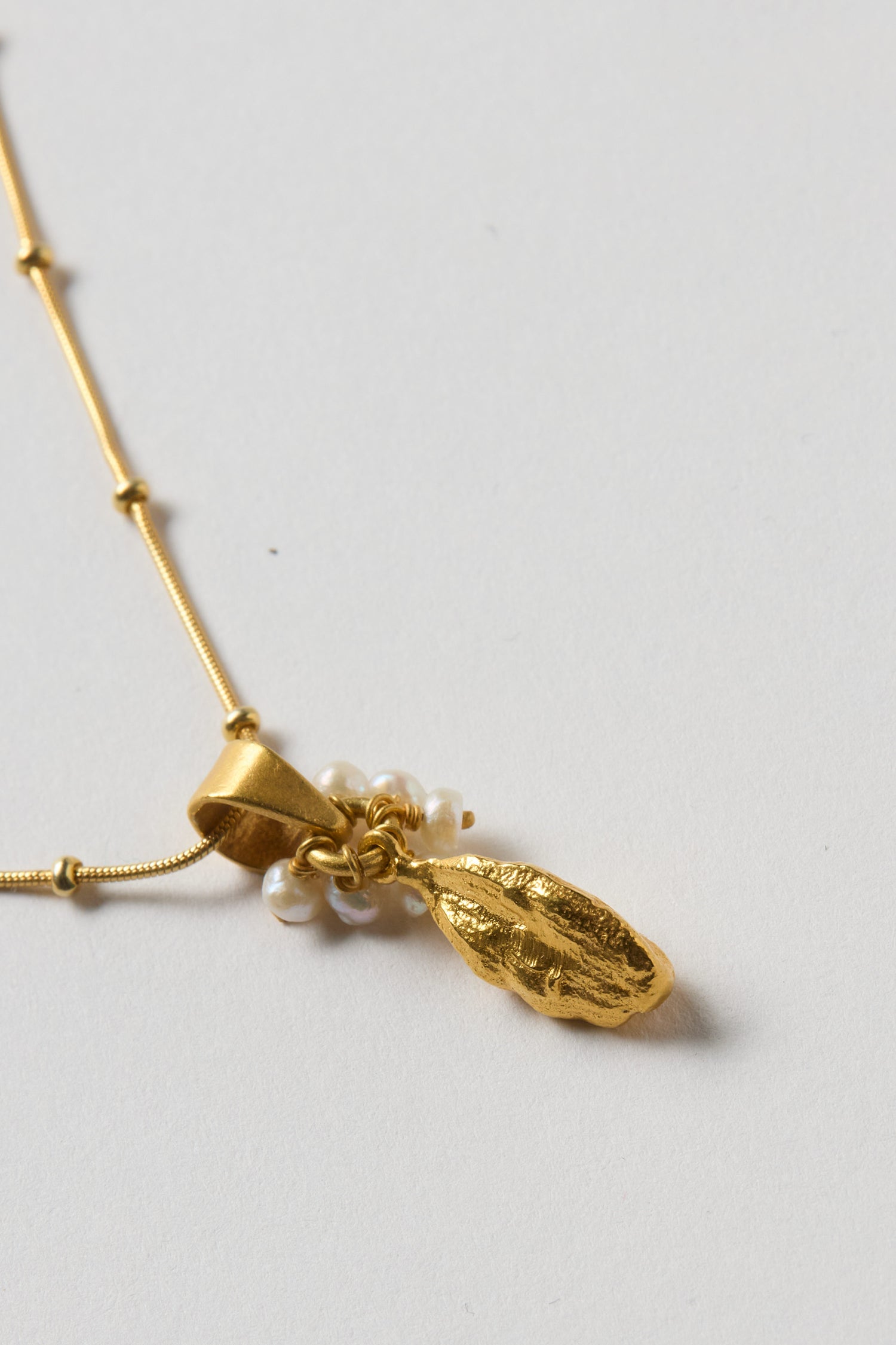 The Gold Vermeil Pearl Drop Necklace features a textured gold leaf pendant and small freshwater pearls, creating an elegant accessory that stands out beautifully against light backgrounds.