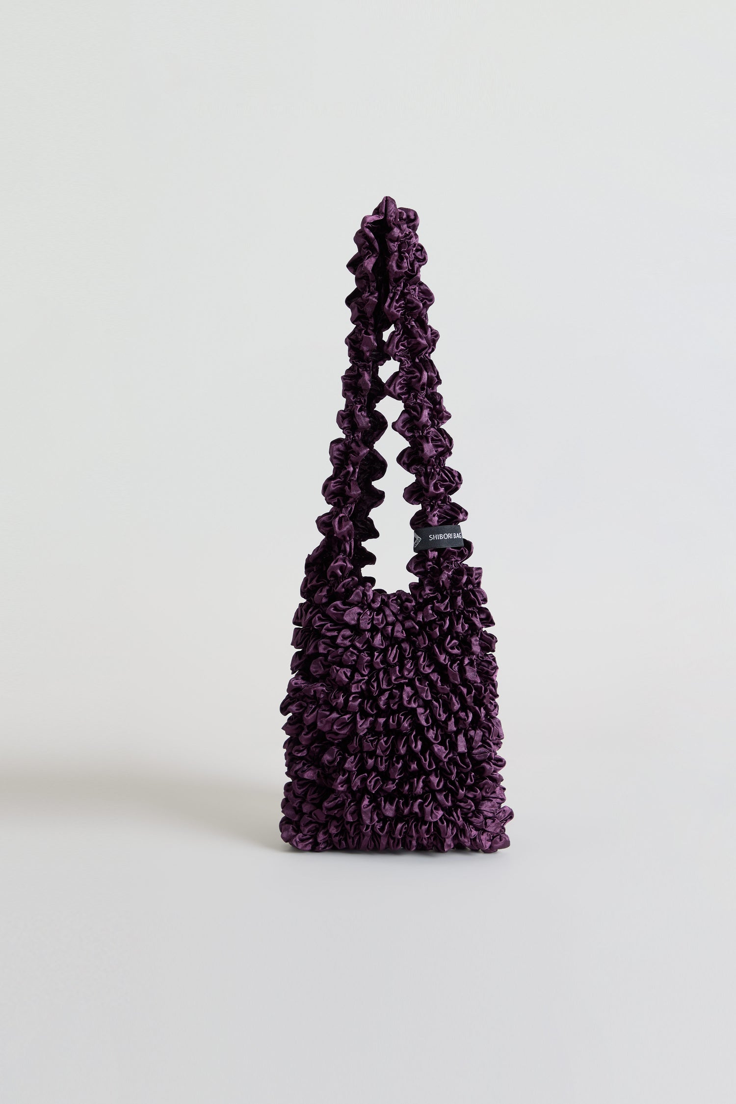 Aubergine Shibori Pleated bag in deep purple with a ruched, gathered texture and a single continuous strap.