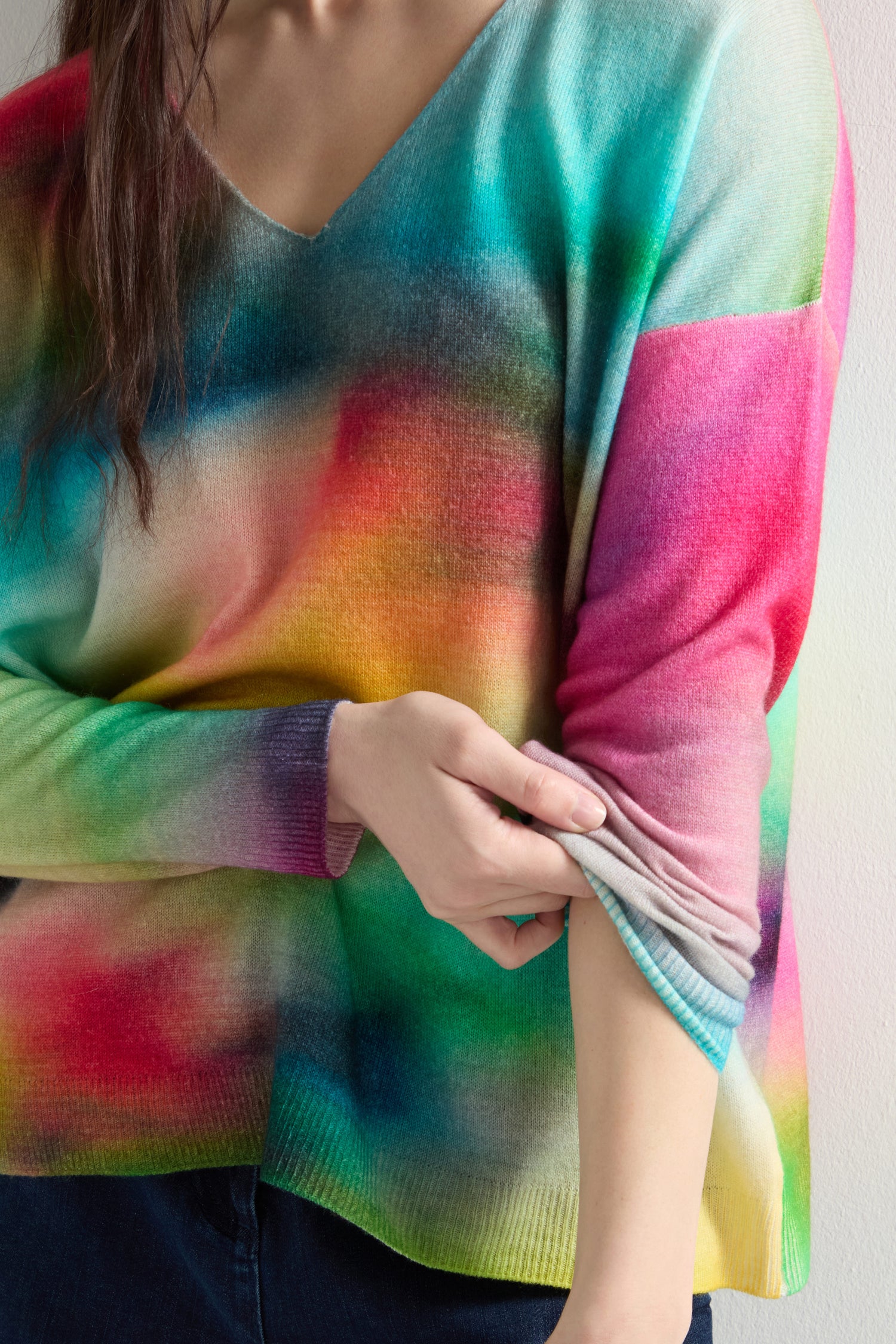 A person in a V-Neck Cashmere Jumper with a colorful, abstract rainbow watercolor print is adjusting the drop shoulder design sleeve with their left hand.