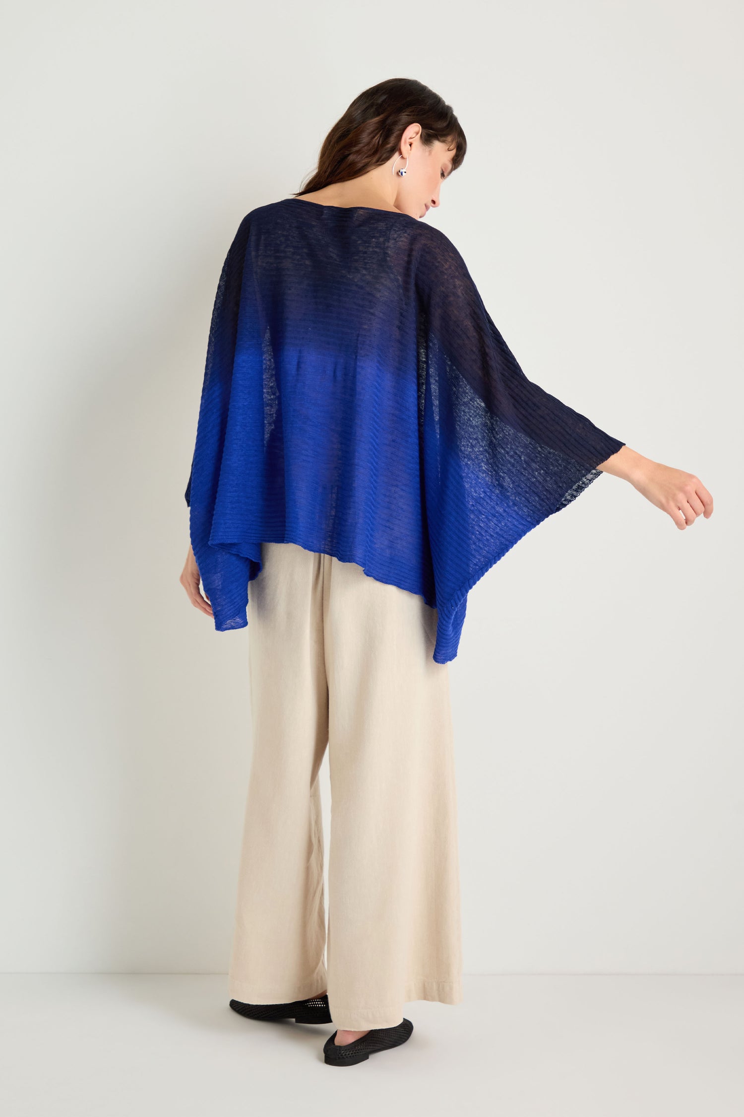 A person stands facing away, wearing the Navy Blue Dip Dye Knit Easy Top with wide sleeves and light-colored wide-leg pants, highlighting a relaxed silhouette against a plain background.