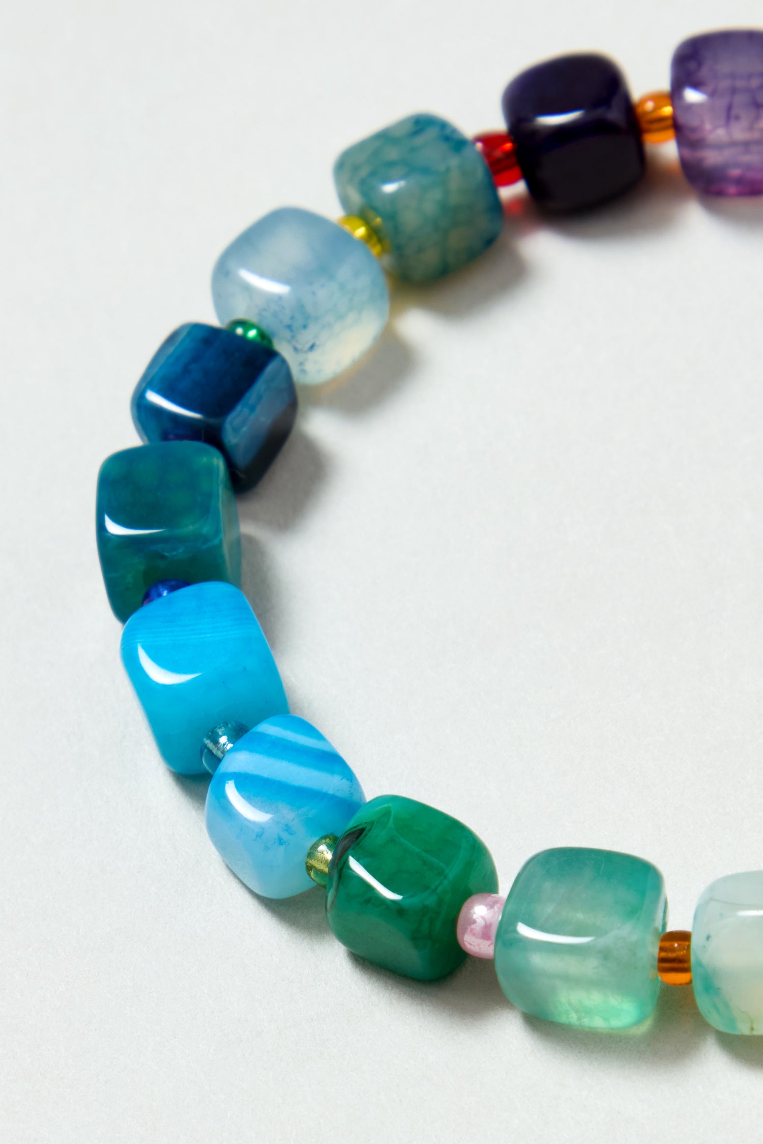 A close-up of the Artisanal Rainbow Agate Bead Bracelet, handmade in Scotland, featuring square multicolored agate beads in blue, green, purple, and pink tones on a light background.