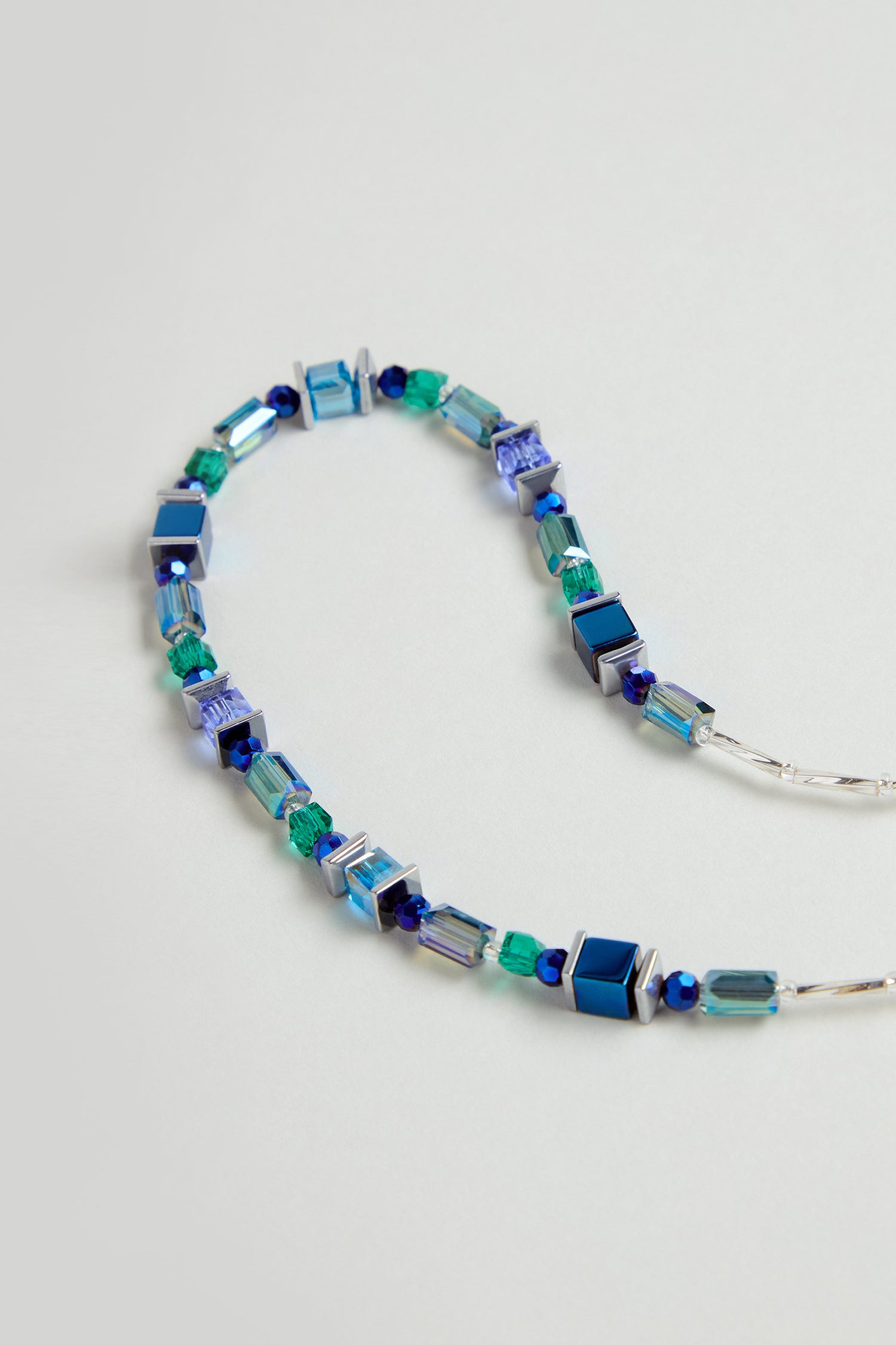 The Blue Hematite Necklace is handmade in Scotland with square and cylindrical blue, green, and silver beads plus faceted glass crystals, all arranged in a repeating pattern.