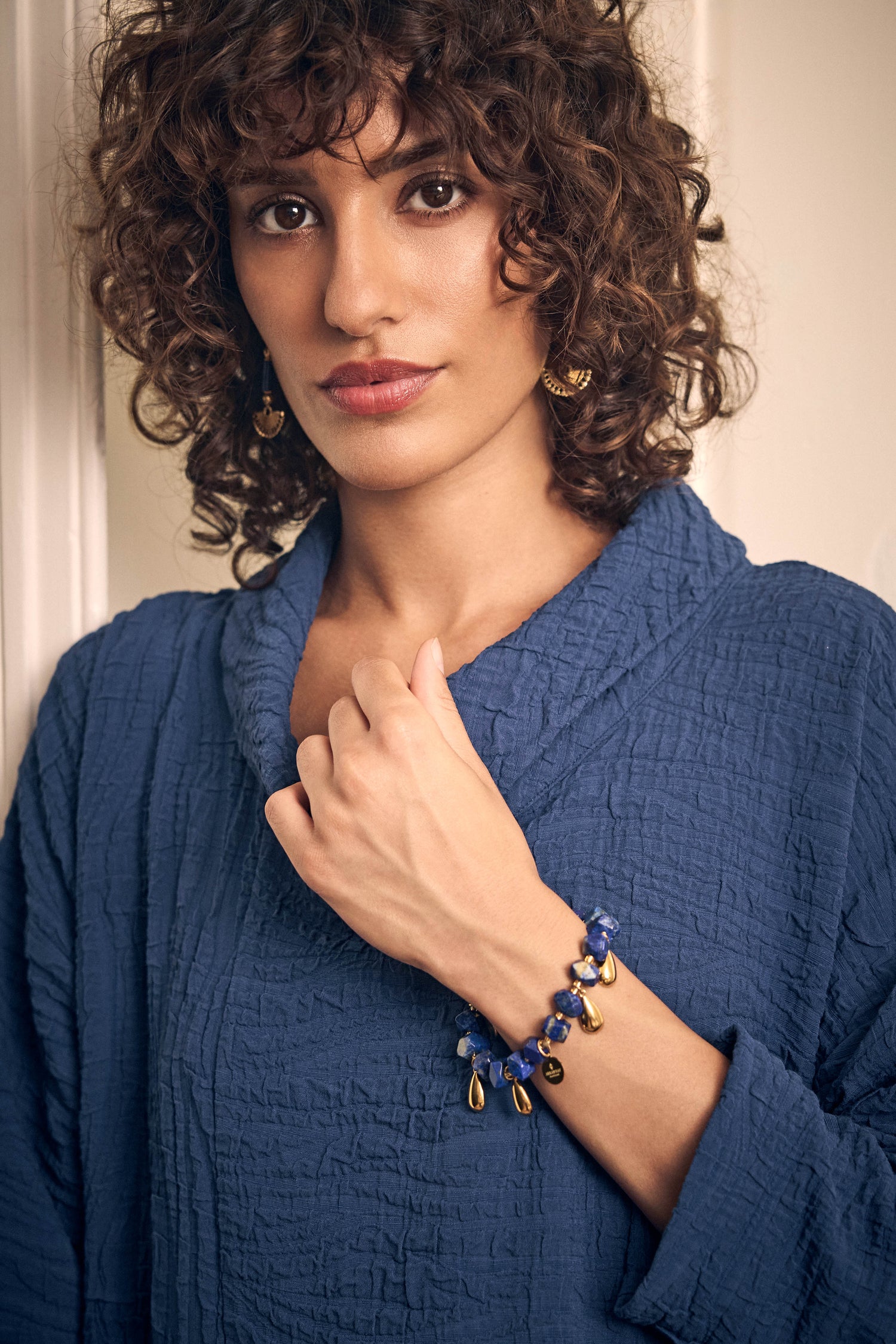 A person wearing a handmade Lapis Lazuli Teardrop Bracelet featuring blue stone beads and small gold teardrop charms.