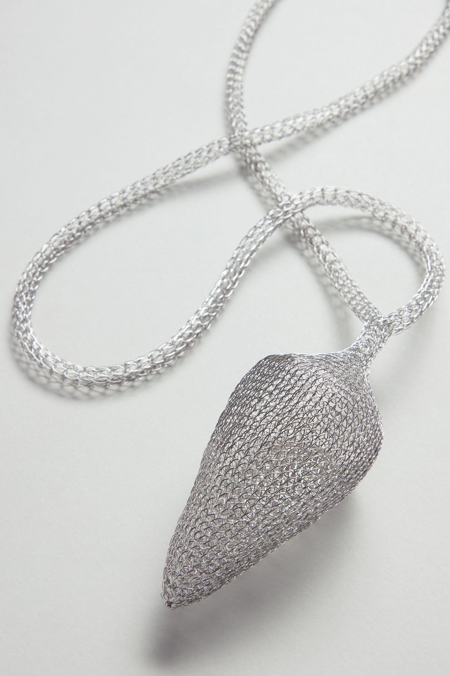 A symbolic jewelry piece, the Silver Hand Crocheted Acorn Necklace features a silver mesh pendant shaped like an acorn and hangs from a matching silver chain, displayed on a light background.