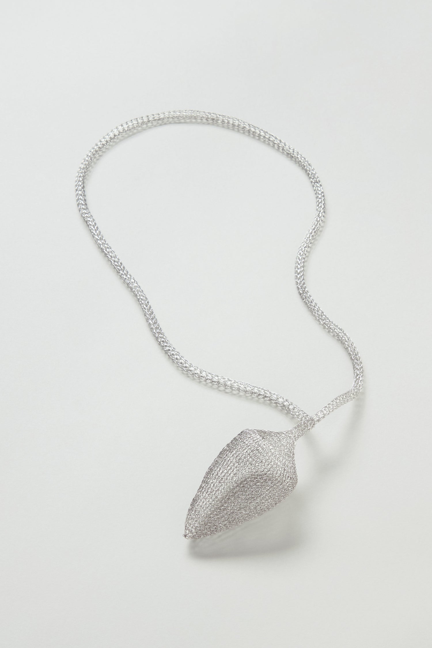 A Silver Hand Crocheted Acorn Necklace features a delicate, textured stainless steel acorn pendant, showcased against a plain light background.