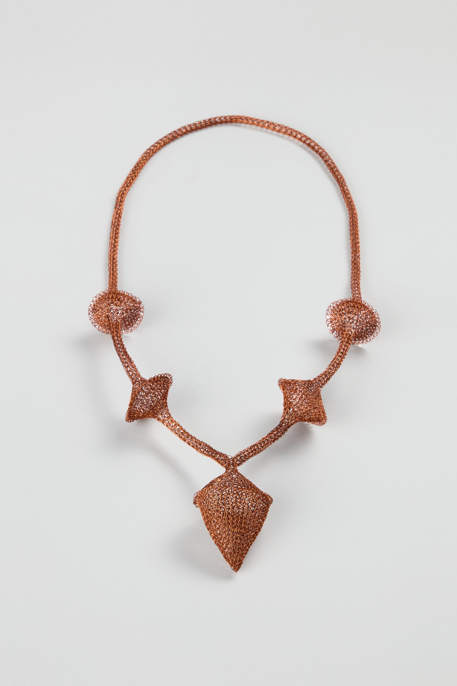 The Hand Crocheted Snowdrop Necklace features a brown cord and symmetrical arrangement of two spherical and three diamond-shaped beaded ornaments.