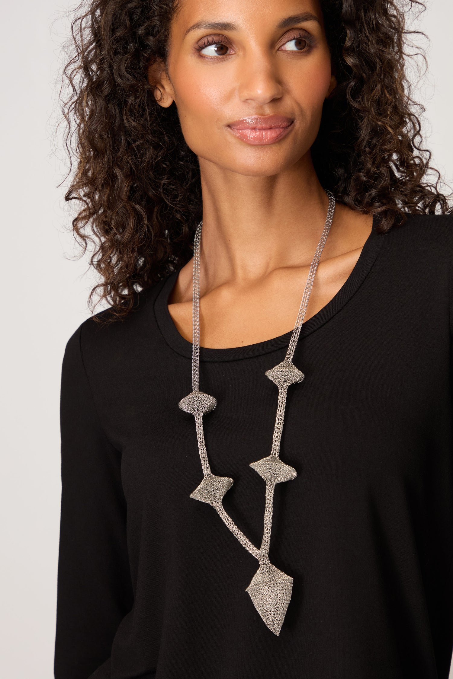 Woman with curly hair wearing a black top and a Hand Crocheted Snowdrop Necklace, looking slightly to the side.