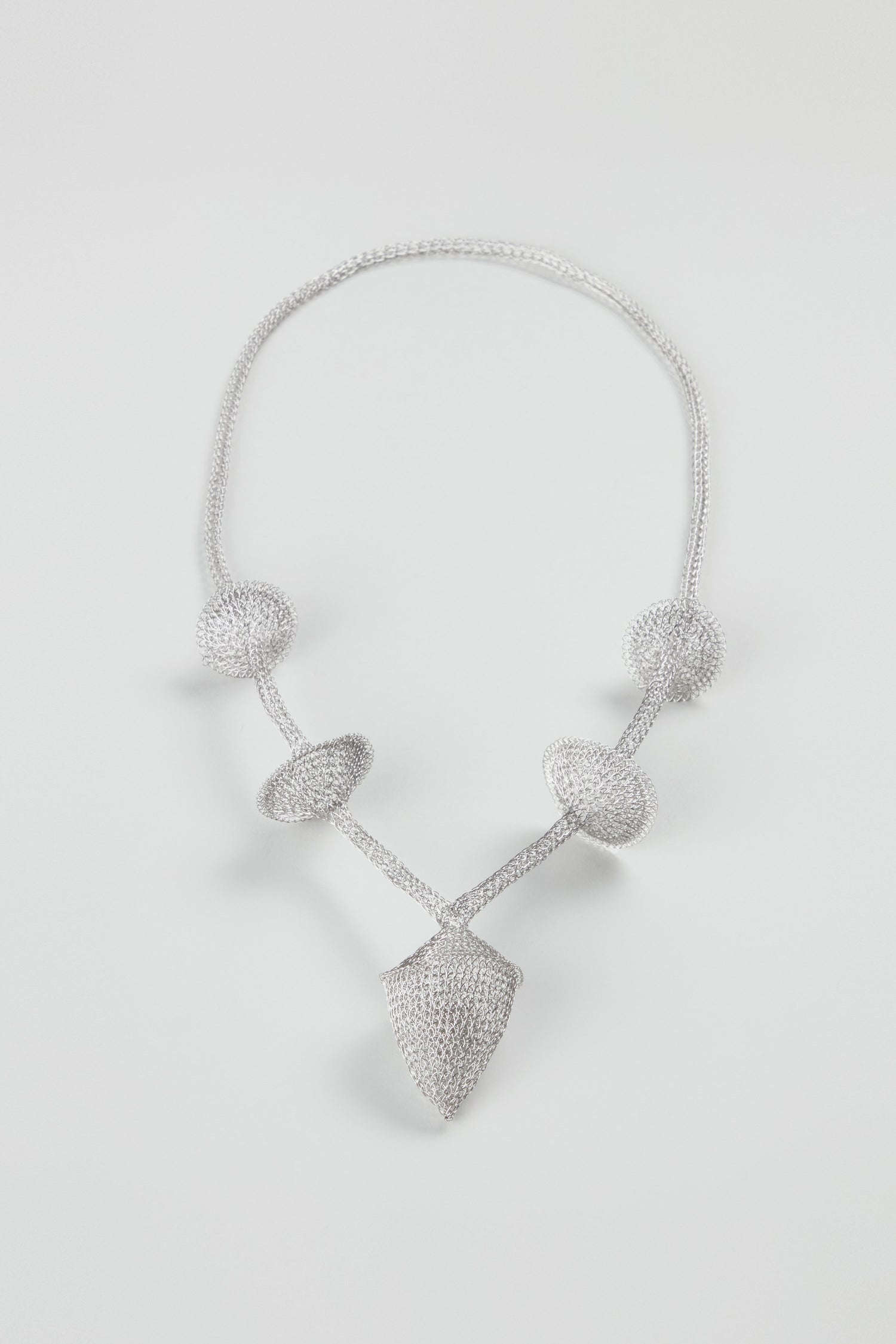 Hand Crocheted Snowdrop Necklace featuring textured geometric shapes—three spheres, a ring, and a shield-like pendant—crafted in stainless steel, displayed on a plain white background.