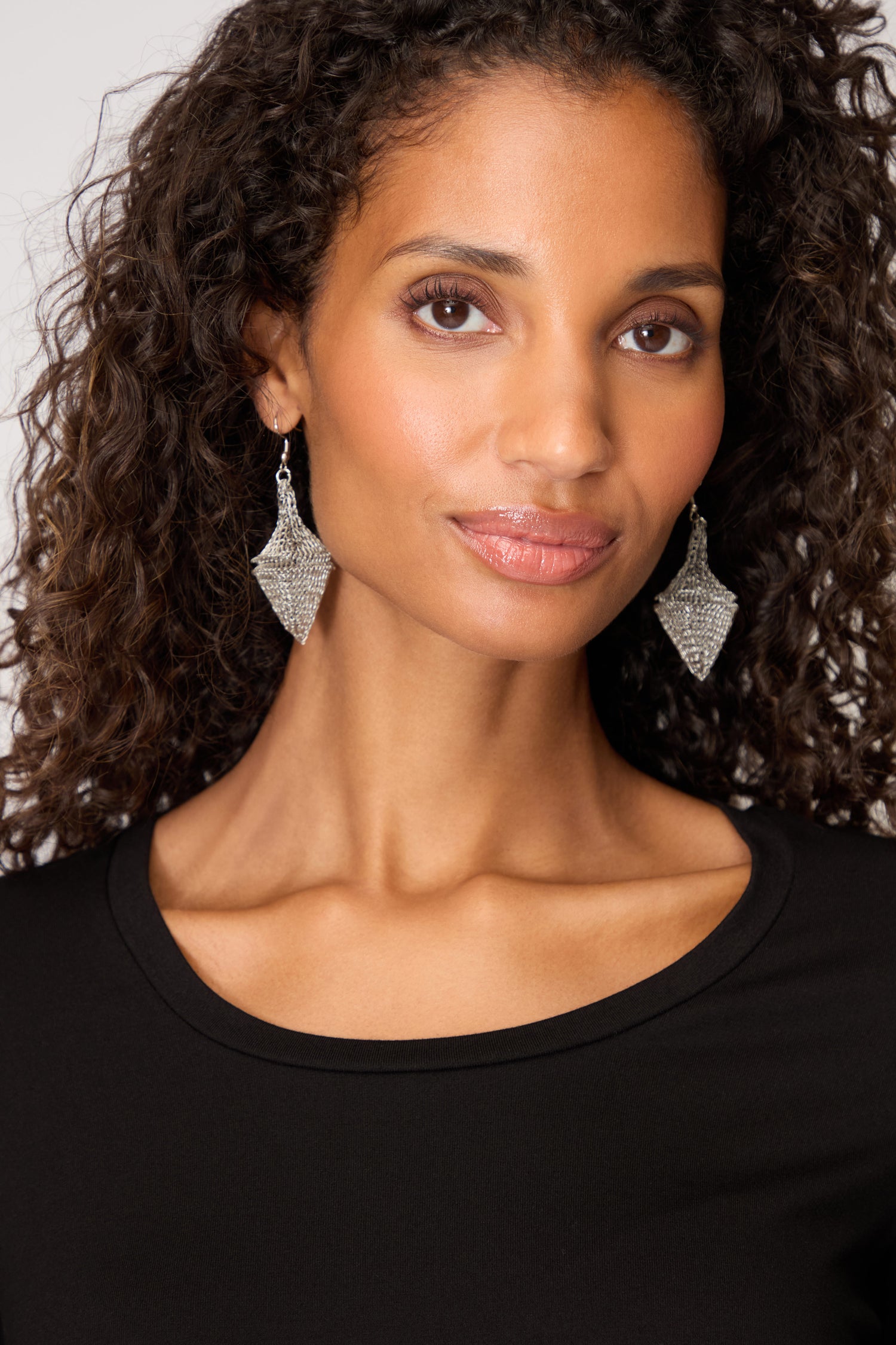A woman with curly hair wears a black top and Hand Crocheted Earrings, looking directly at the camera with a neutral expression.