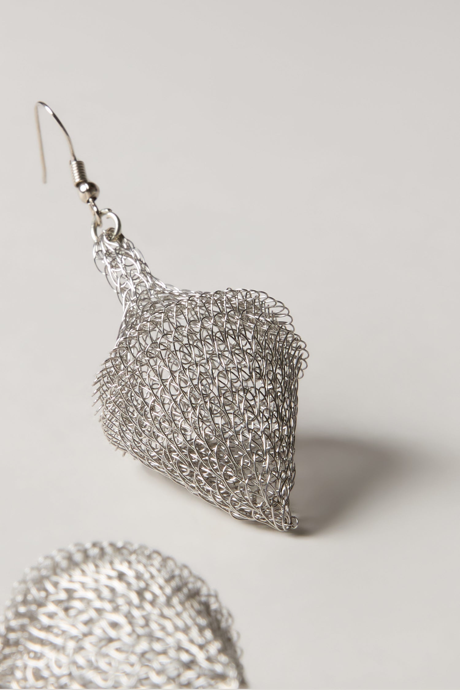 Close-up of a Hand Crocheted Earring with a silver wire mesh teardrop design on a neutral background. Another similar stainless steel Hand Crocheted Earring is partially visible in the foreground.