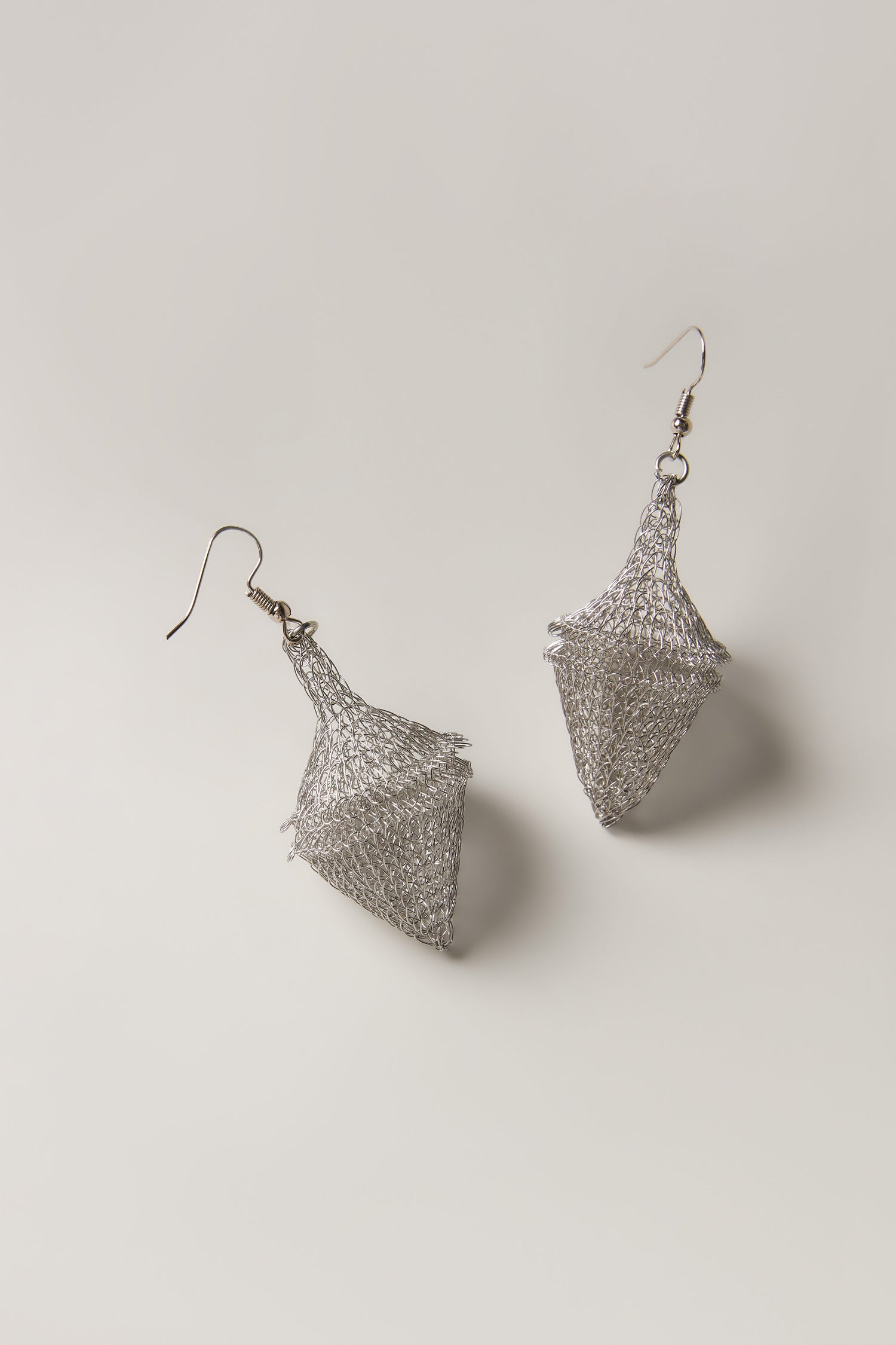 The Hand Crocheted Earrings feature a pair of silver wire mesh in geometric diamond shapes, showcased on a simple light background.