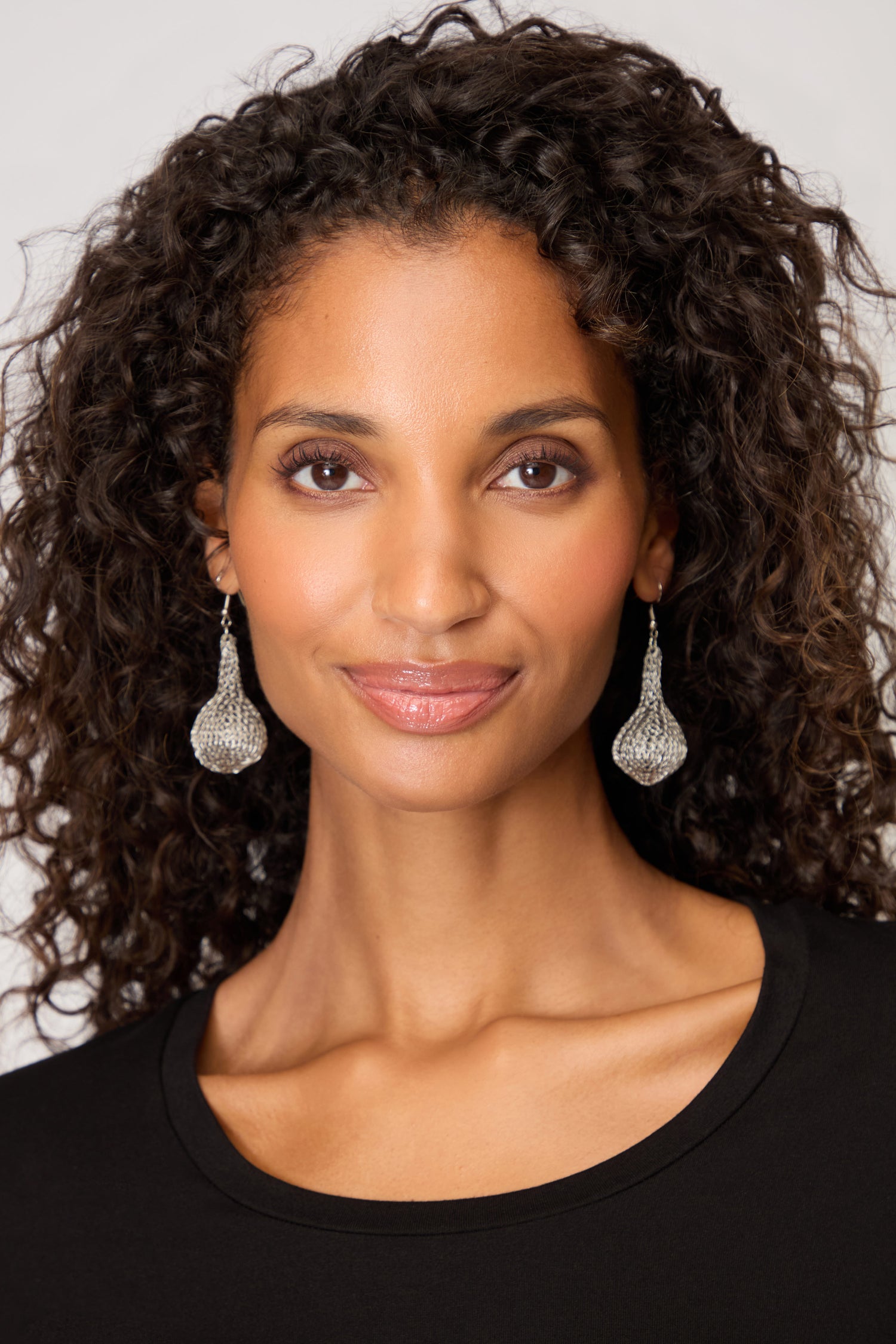 A woman with curly hair wears Hand Crocheted Teardrop Earrings and a black top, smiling slightly against a plain background.
