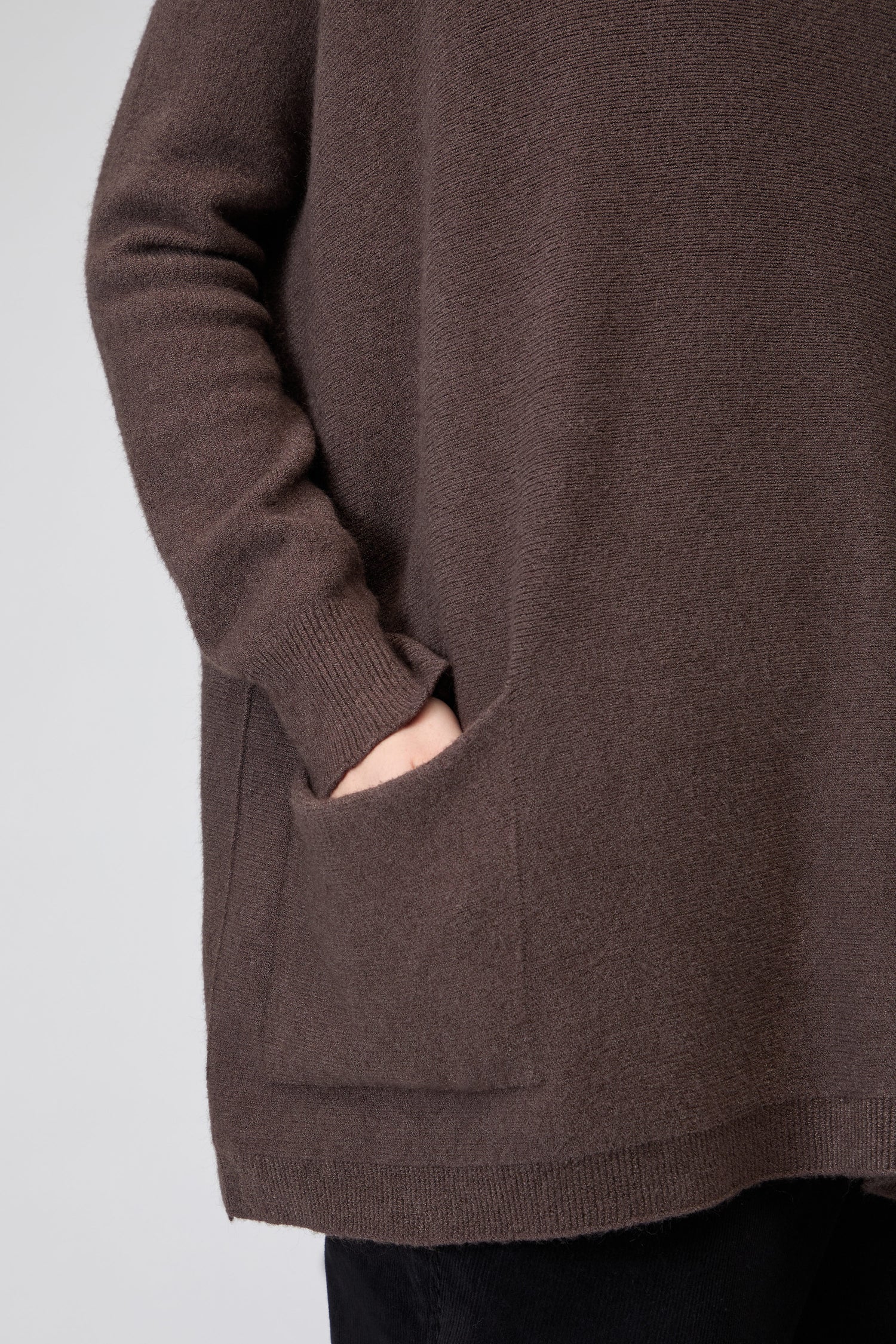 A woman wearing the Two Pocket Oversize Knit, an ultra-cozy, supersoft jumper with her right hand in one of the front pockets, shown from shoulder to hip—perfect for comfortable, relaxed style.