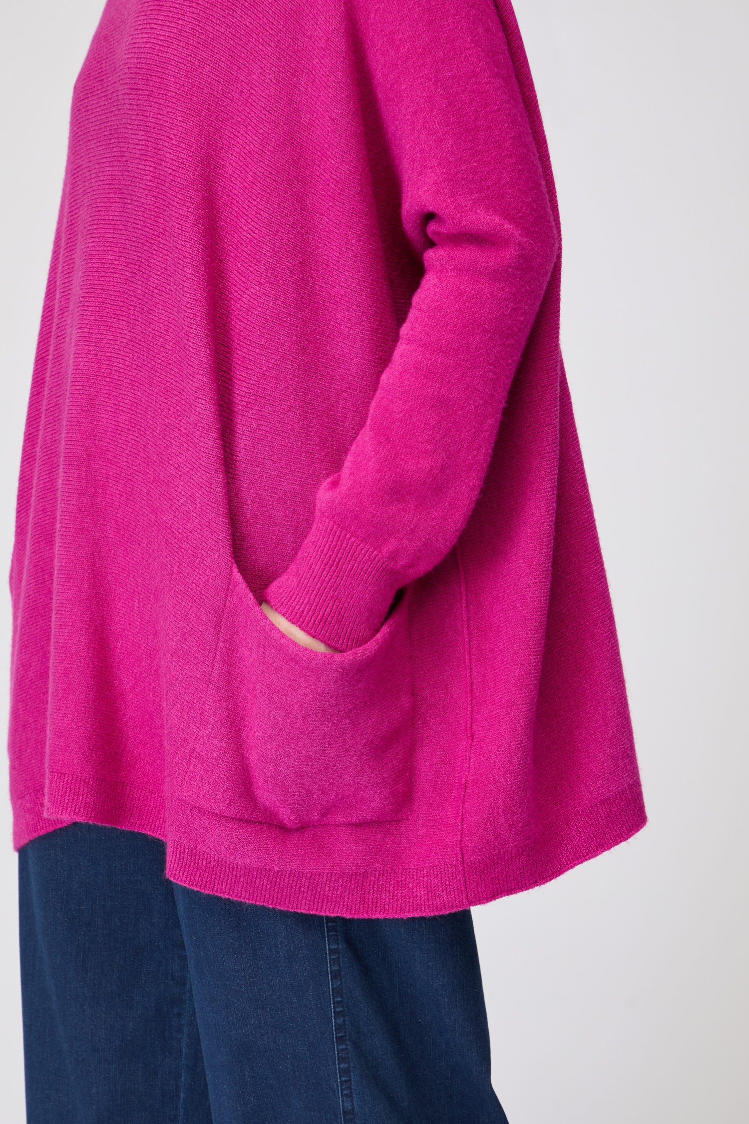 A person wears the Two Pocket Oversize Knit in bright pink, with one hand in a pocket, paired with dark blue pants, shown from shoulders to hips.