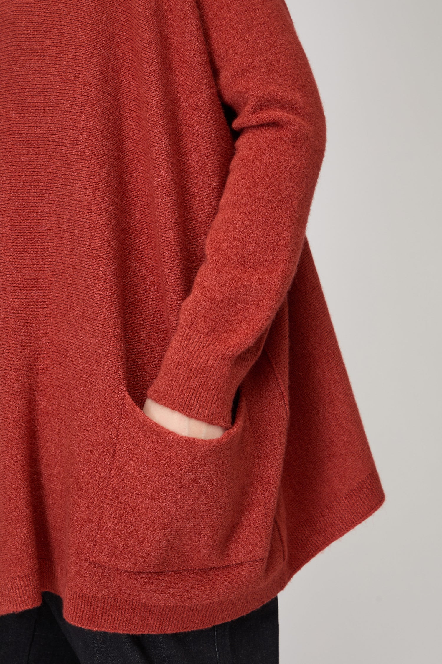 A person wearing the Amazing Woman Two Pocket Oversize Knit, a rust-colored, loose-fitting long-sleeve sweater, with one hand in a front pocket.