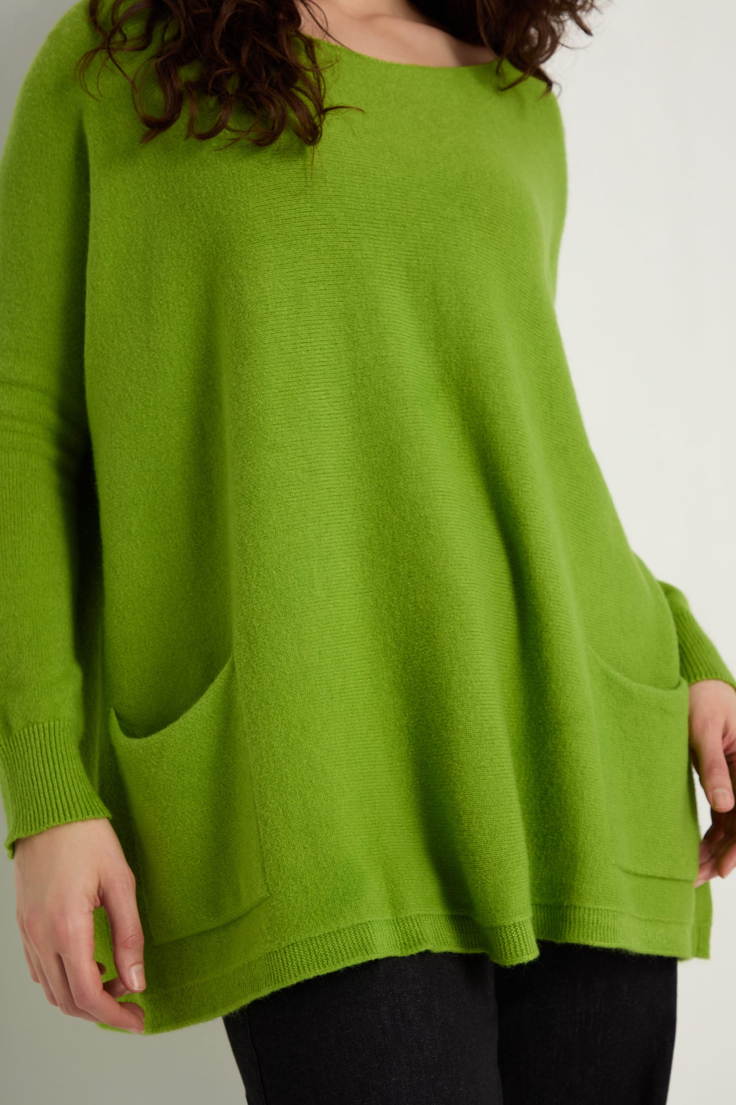 Model wears the Two Pocket Oversize Knit—a green jumper with two front pockets—paired with dark pants, a cozy essential in women's knitwear.