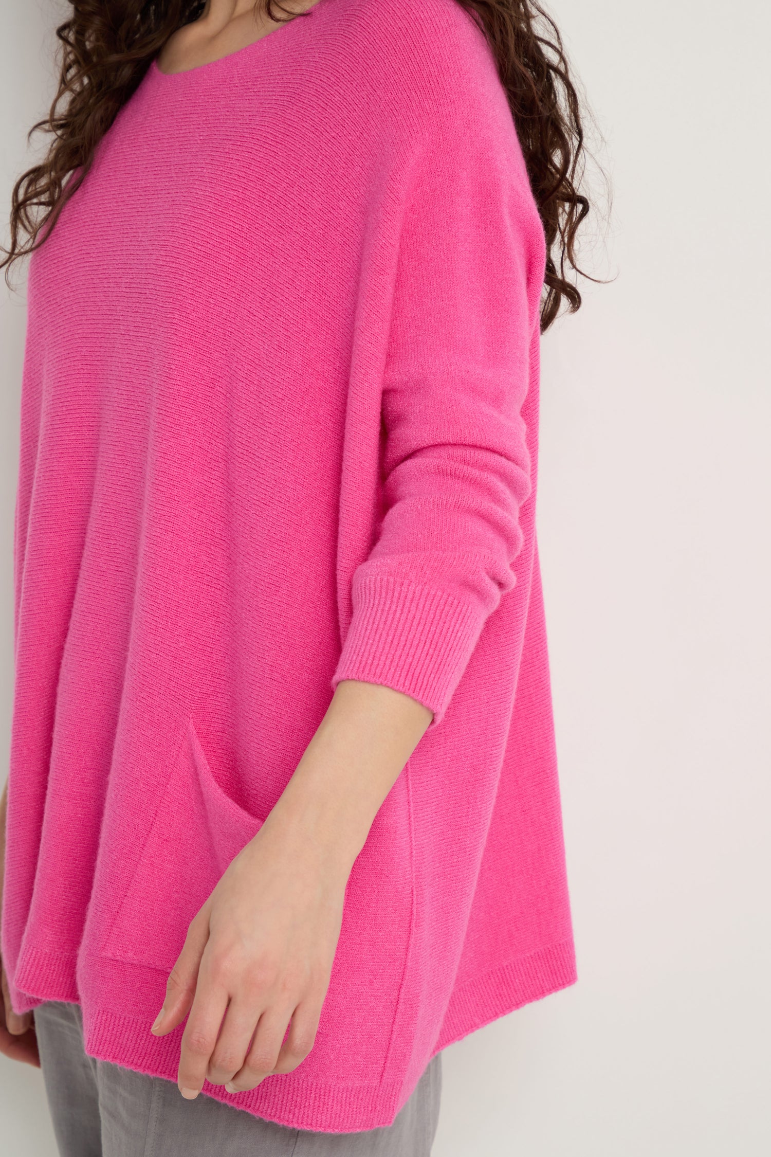 A person wearing a bright pink Two Pocket Oversize Knit jumper with gray pants stands against a white background.